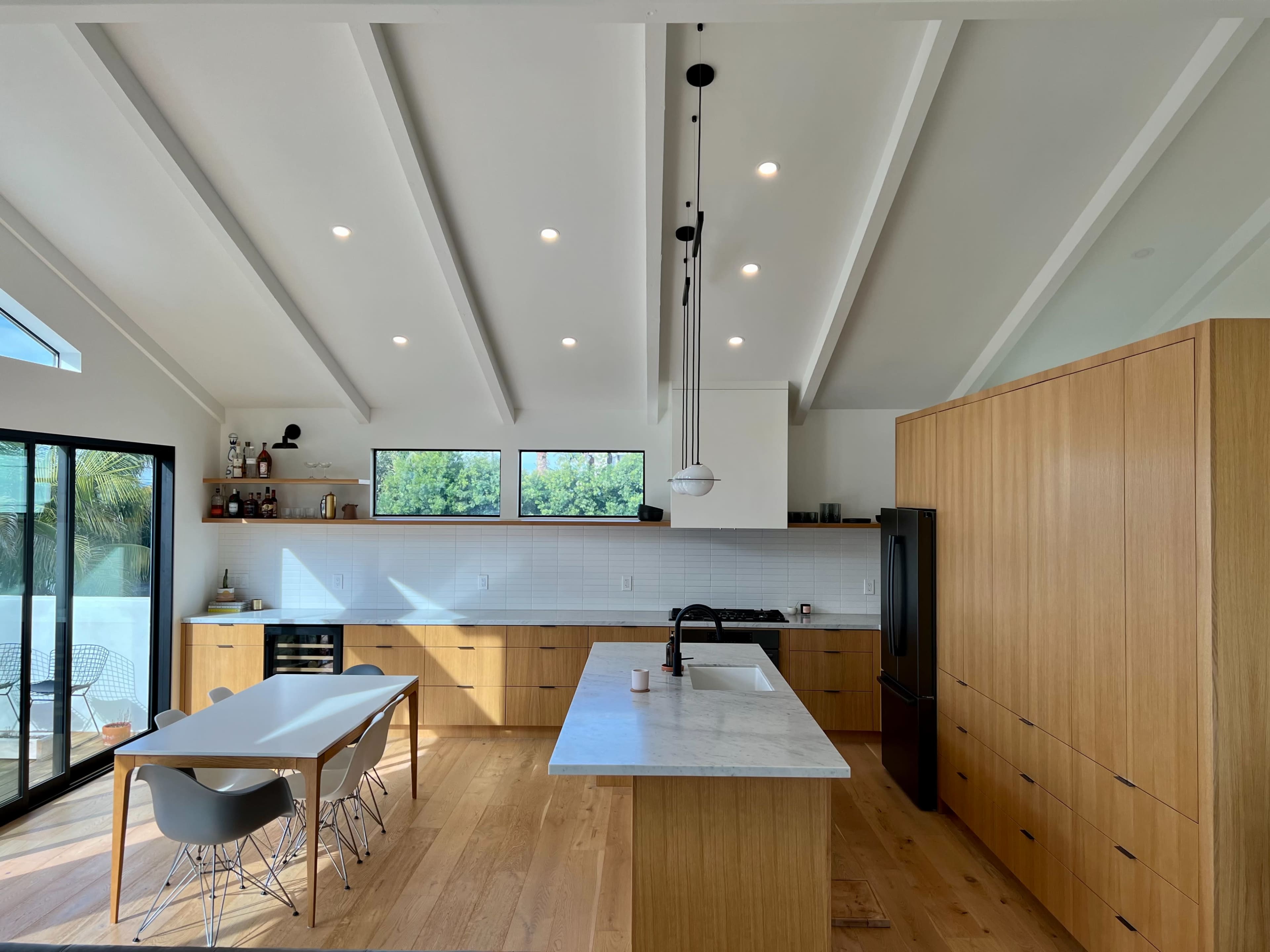 A modern kitchen features wooden cabinetry, a marble island, and large windows illuminating the space.