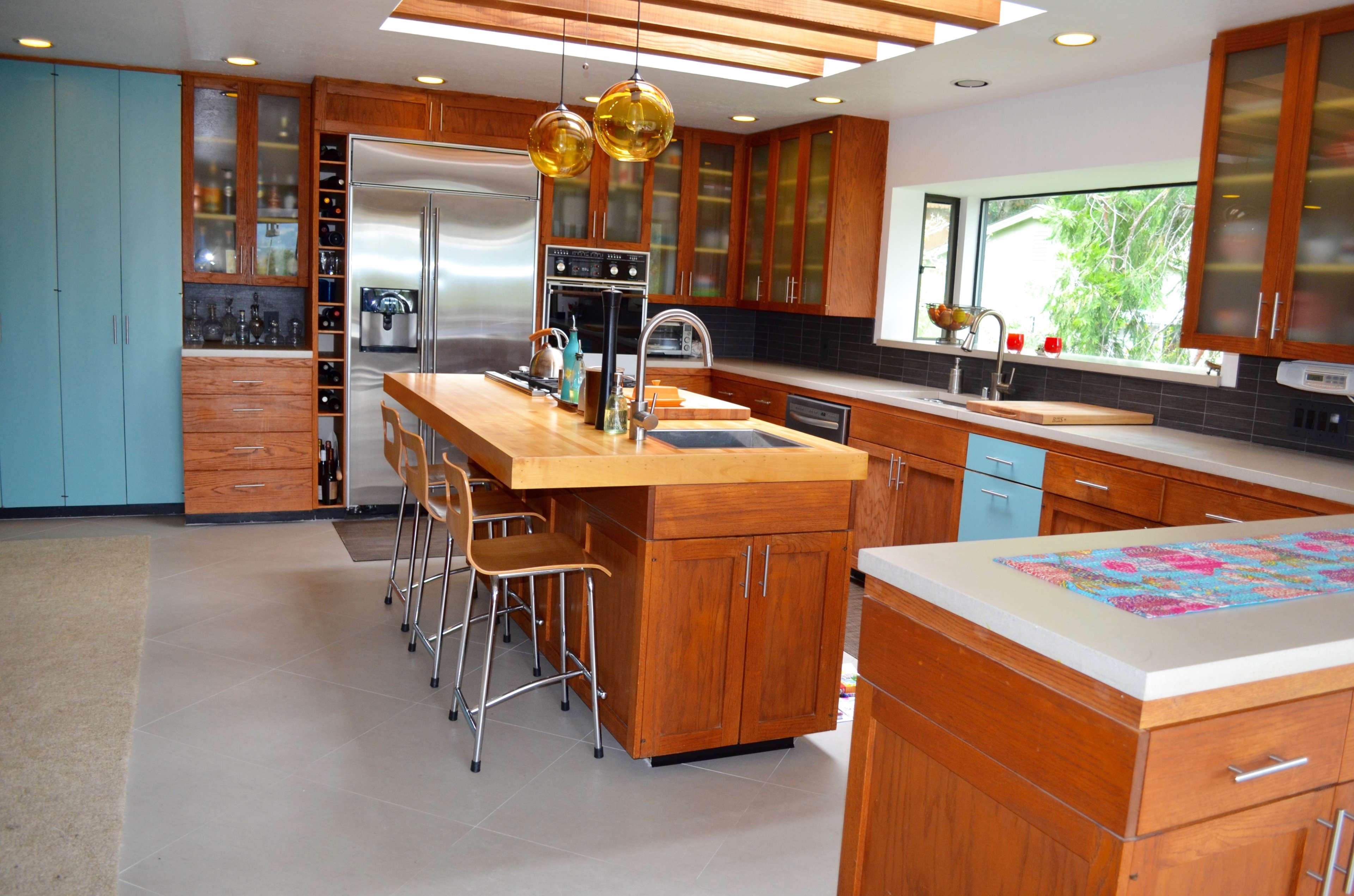 The image shows a modern kitchen with wooden cabinetry, a central island with a sink, and stainless steel appliances.