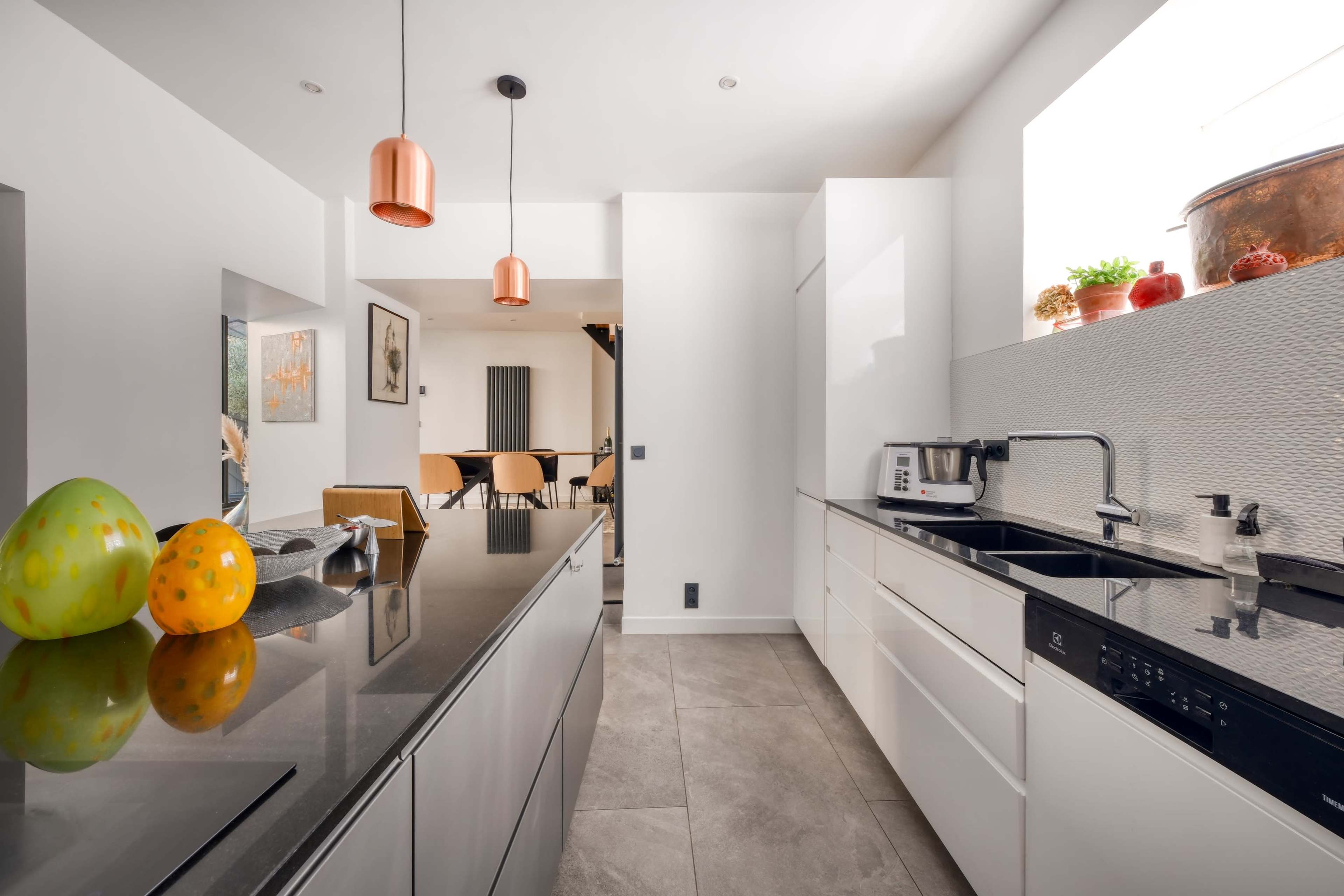 The image shows a modern kitchen with glossy white cabinets, a black countertop, and pendant lighting above the island.