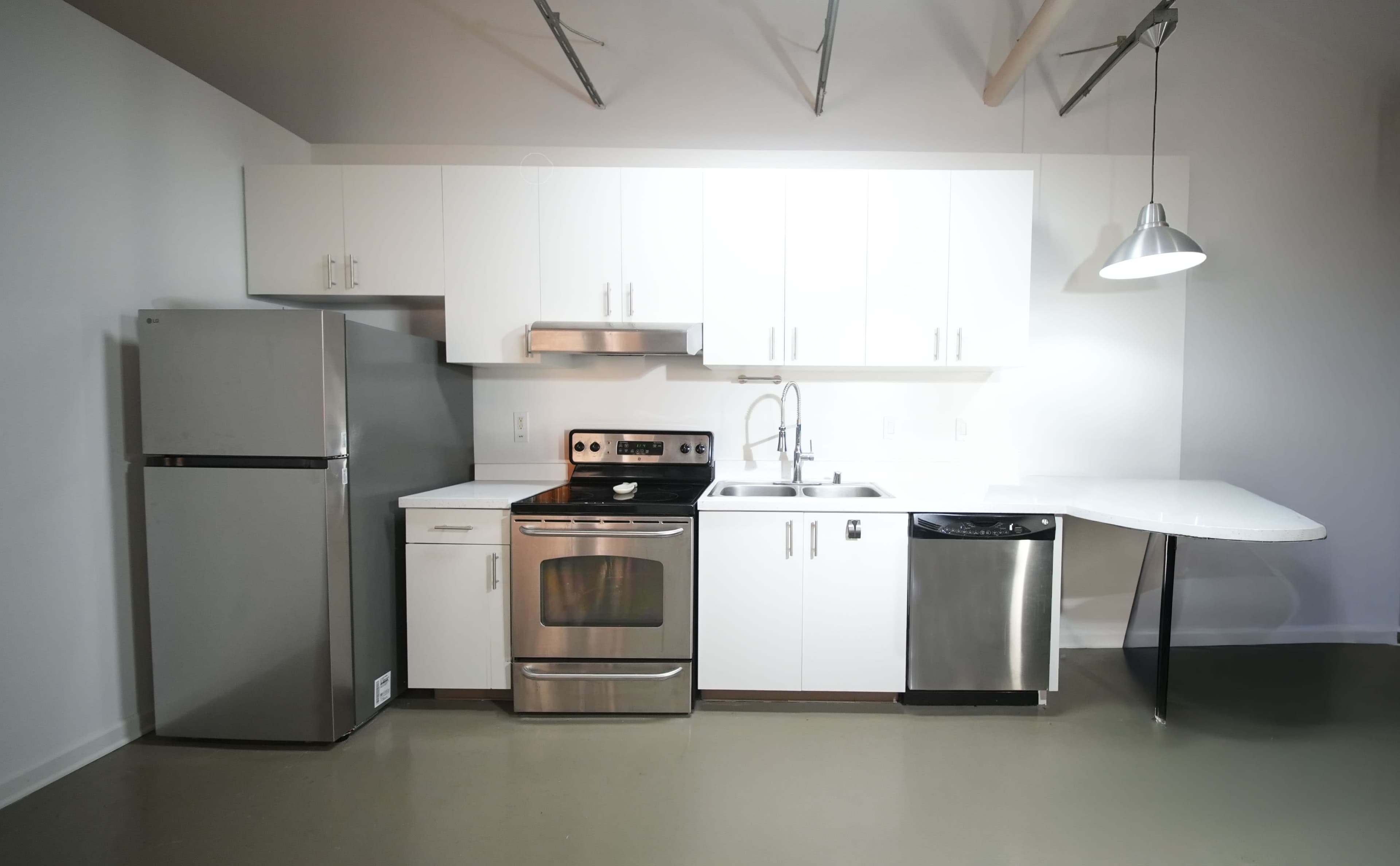 The image features a modern kitchen with stainless steel appliances, including a refrigerator, stove, and dishwasher, complemented by white cabinetry and a simple countertop layout.