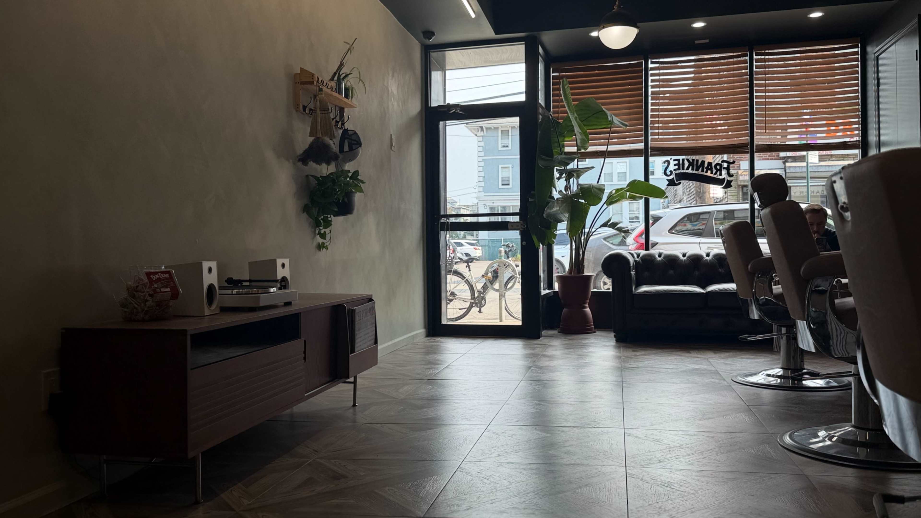 The image shows a modern interior of a salon or waiting area with a brown leather sofa, a plants, and a window displaying outside street views.