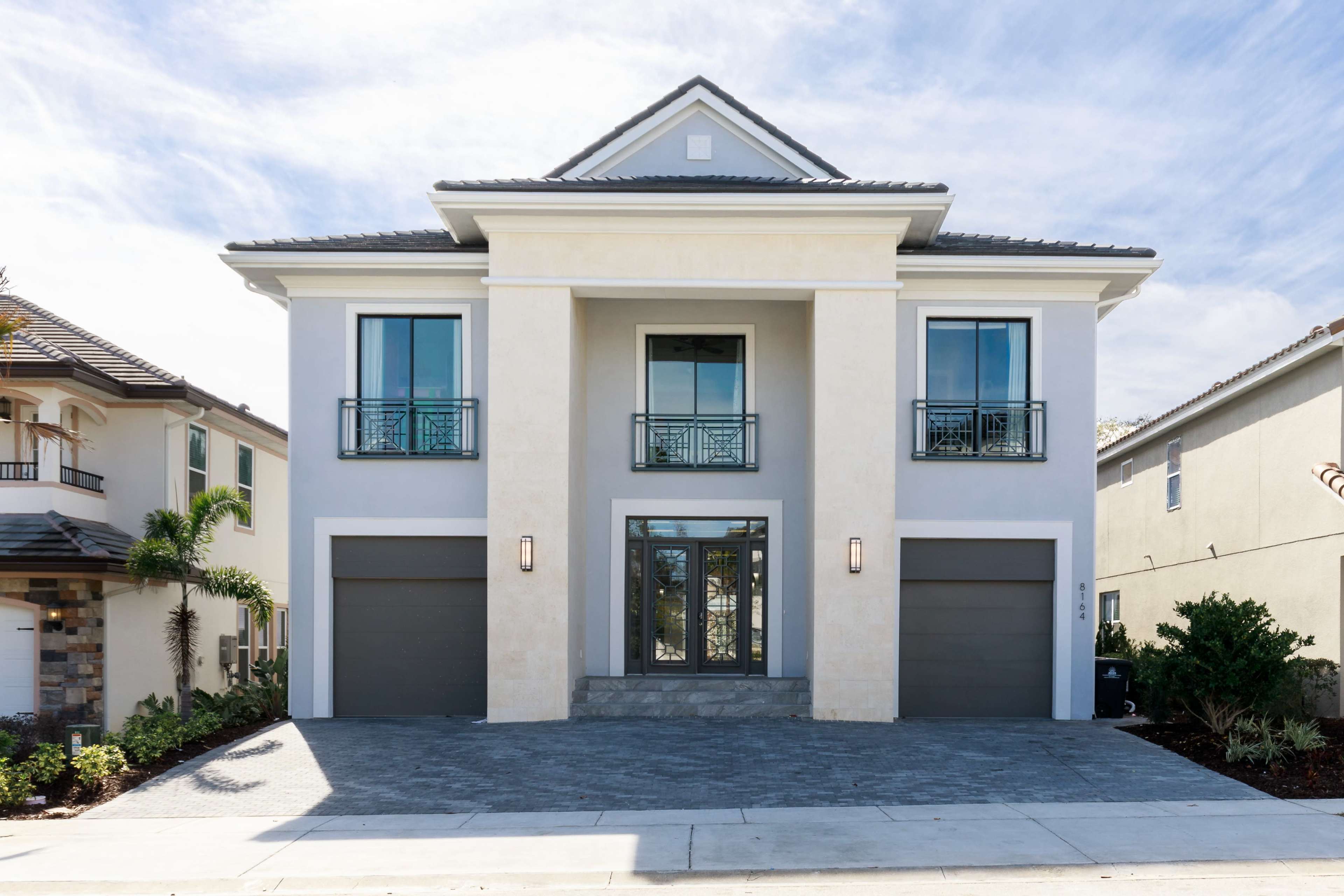 A modern two-story house with a symmetrical façade, featuring large windows and a central entrance, flanked by two garages.