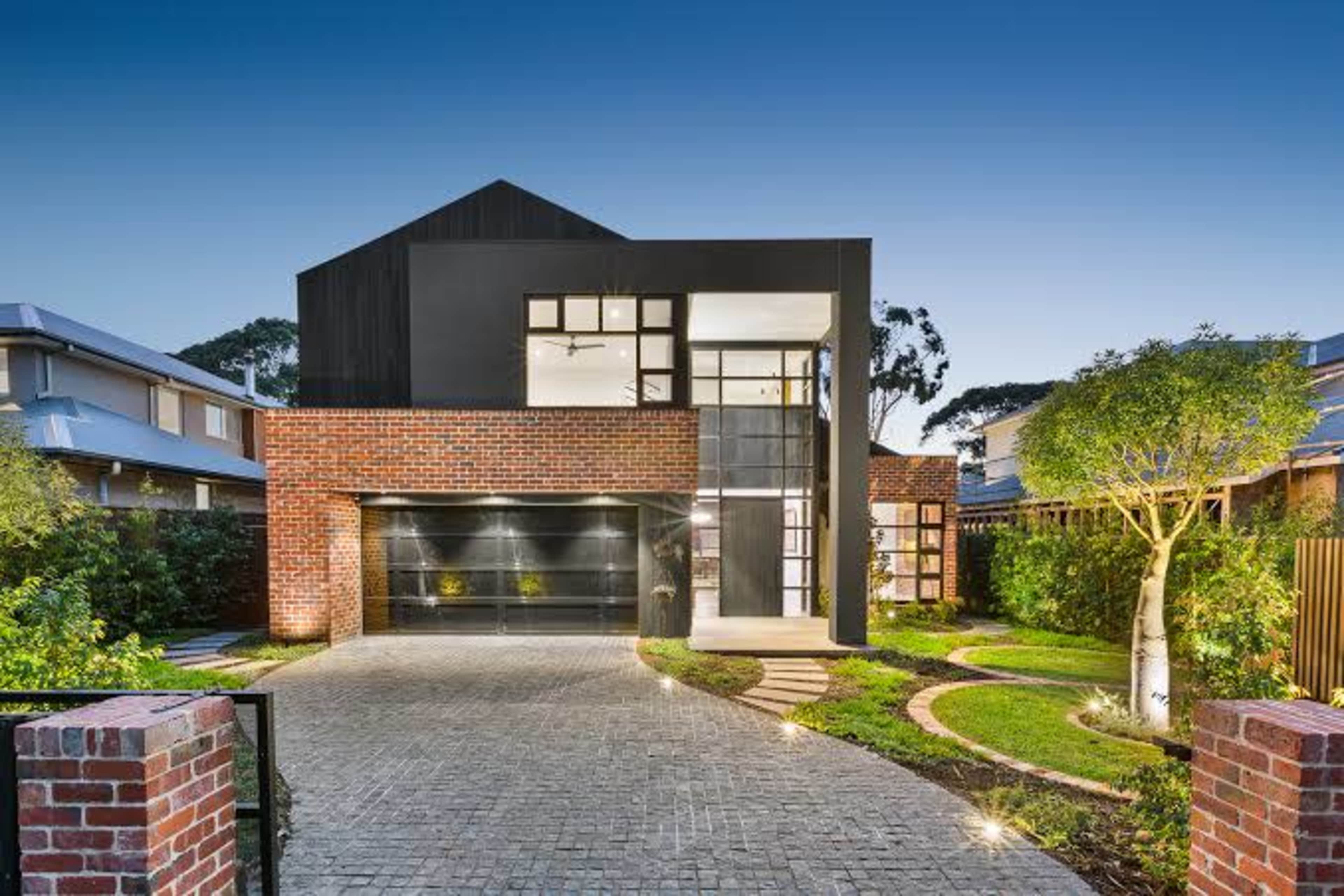 A modern two-story house with a mix of brick and black exterior, surrounded by landscaped greenery and a paved driveway.