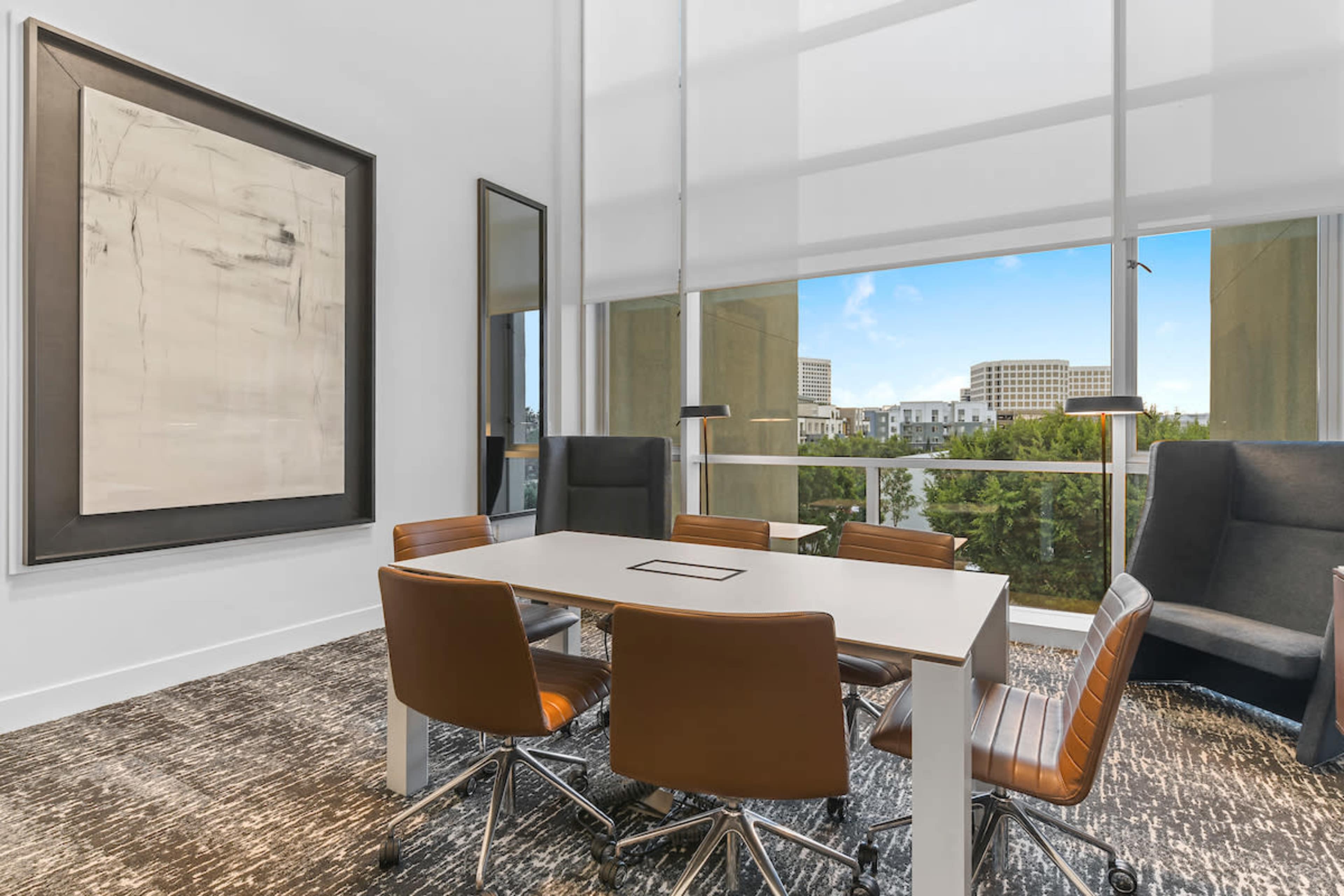 A modern conference room features a rectangular table surrounded by brown leather chairs and large windows overlooking a cityscape.