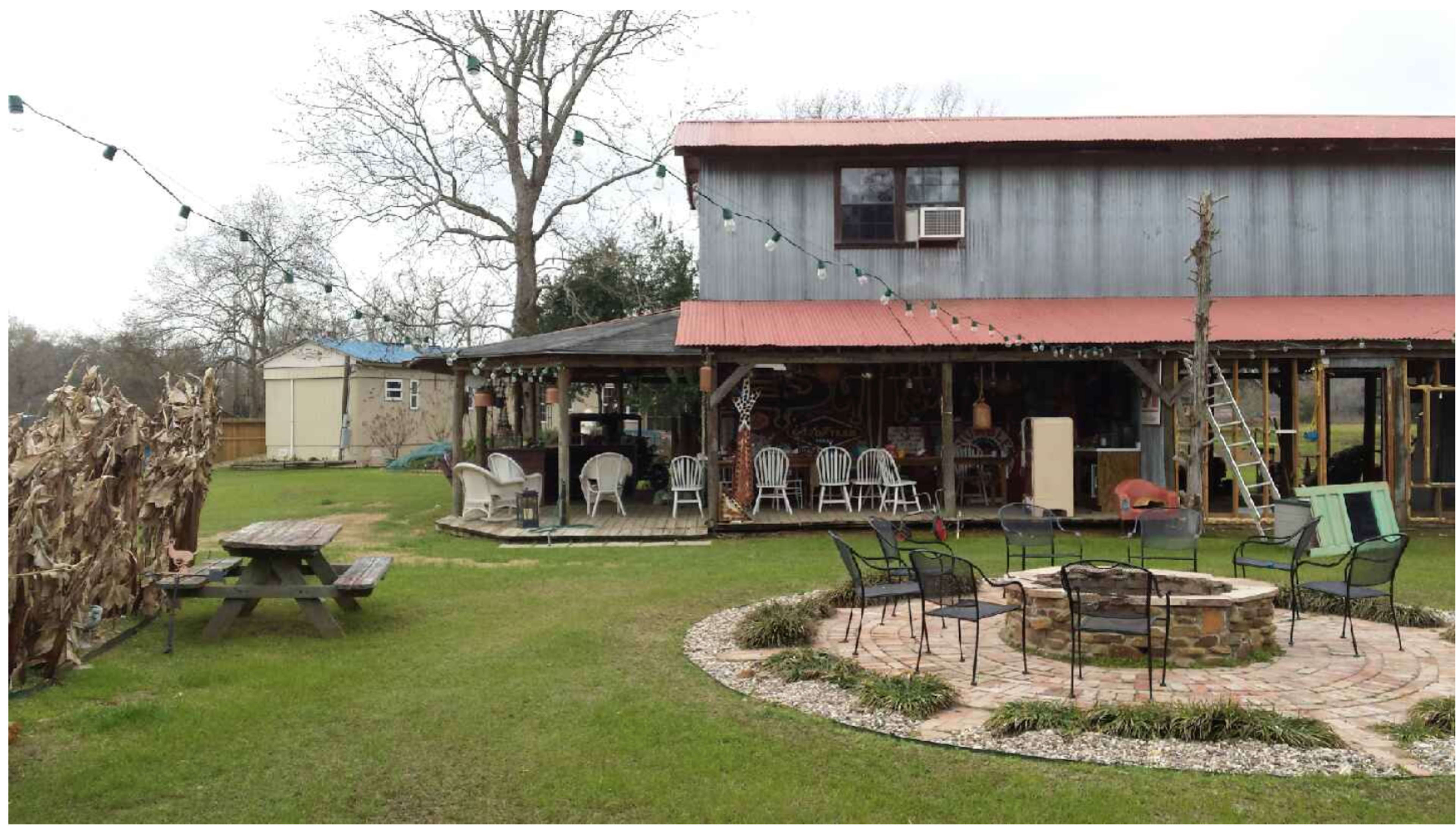 A two-story house with a red roof, surrounded by a grassy yard featuring a picnic table, fire pit, and decorated with string lights.