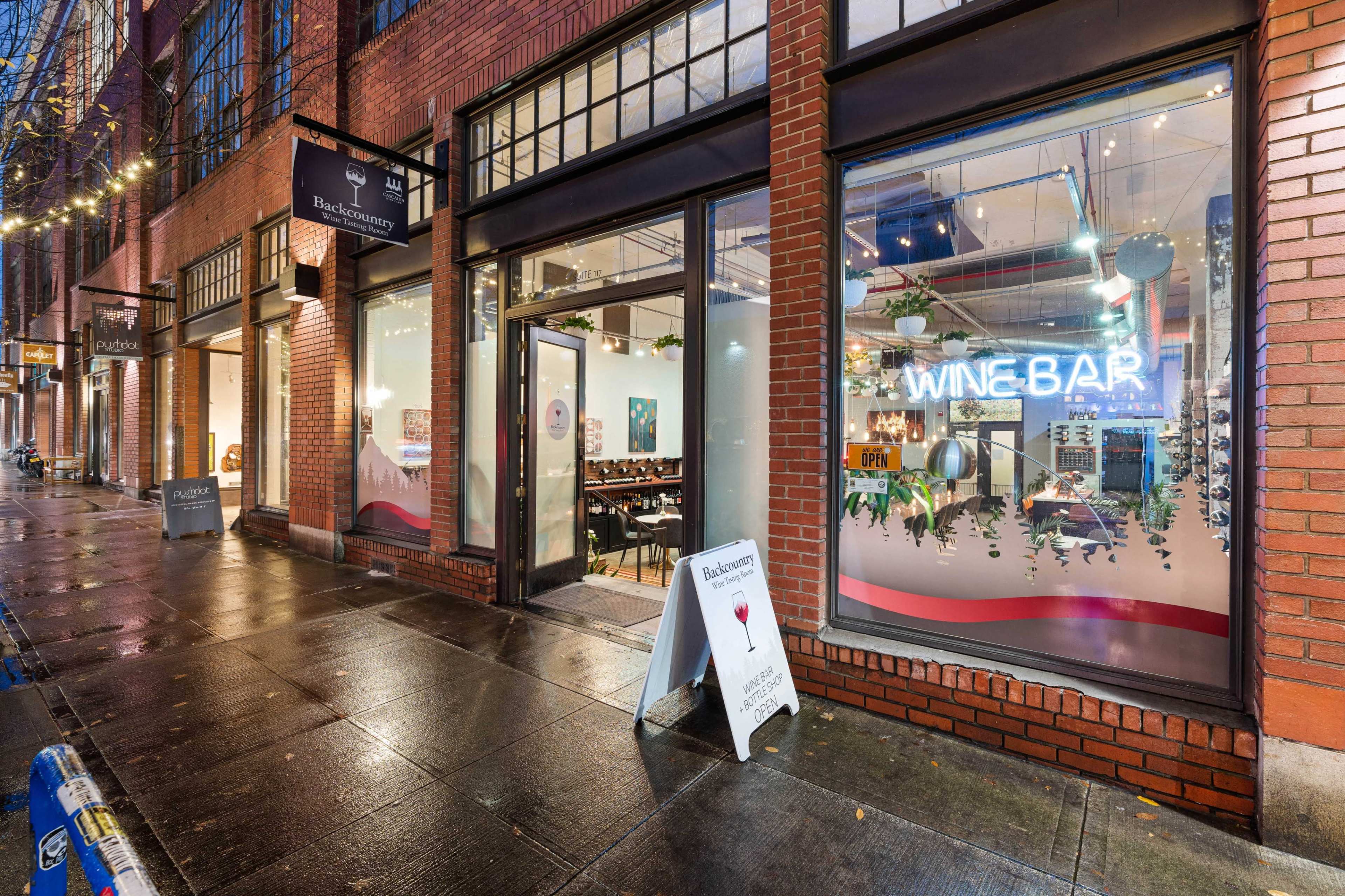 A wine bar with large front windows illuminated by neon lights, located on a brick storefront in a city setting.