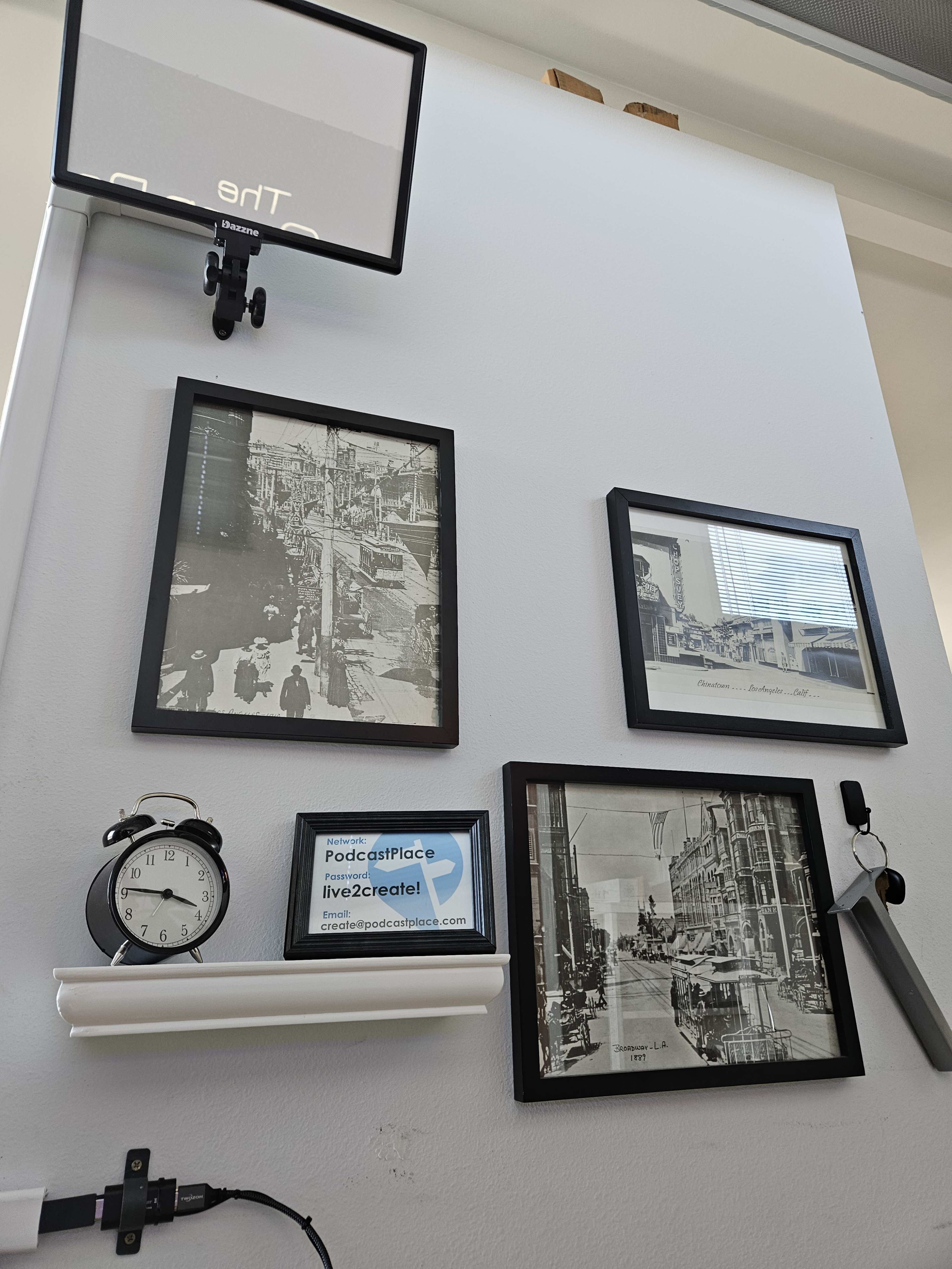 A wall with framed black-and-white photographs, a clock, and a sign featuring the text "Podcast Place live2create.com."