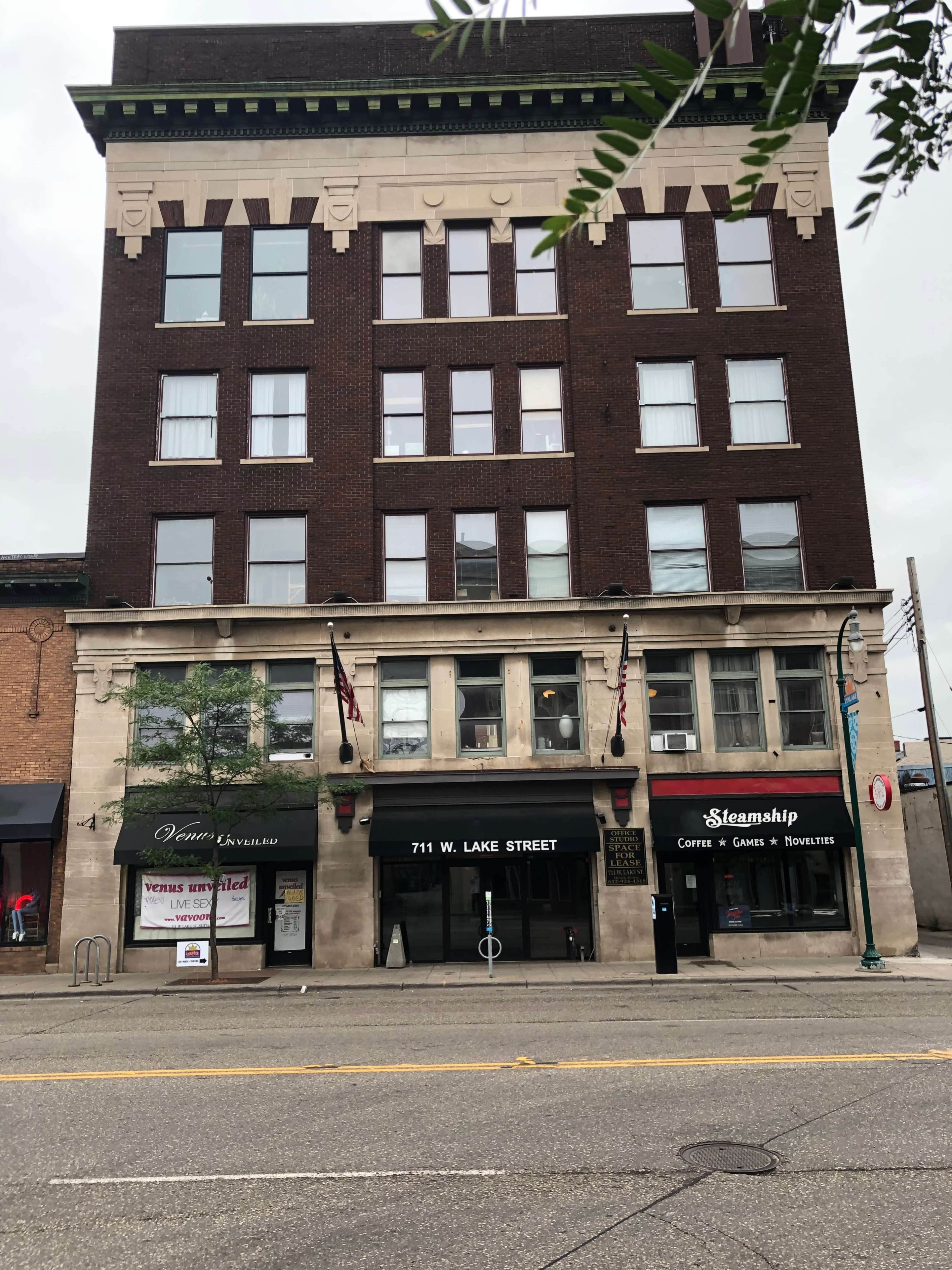 A five-story brick building with large windows, featuring a ground-level storefront labeled "Steamship Coffee & Games" and a sign indicating the address "711 W. Lake Street."