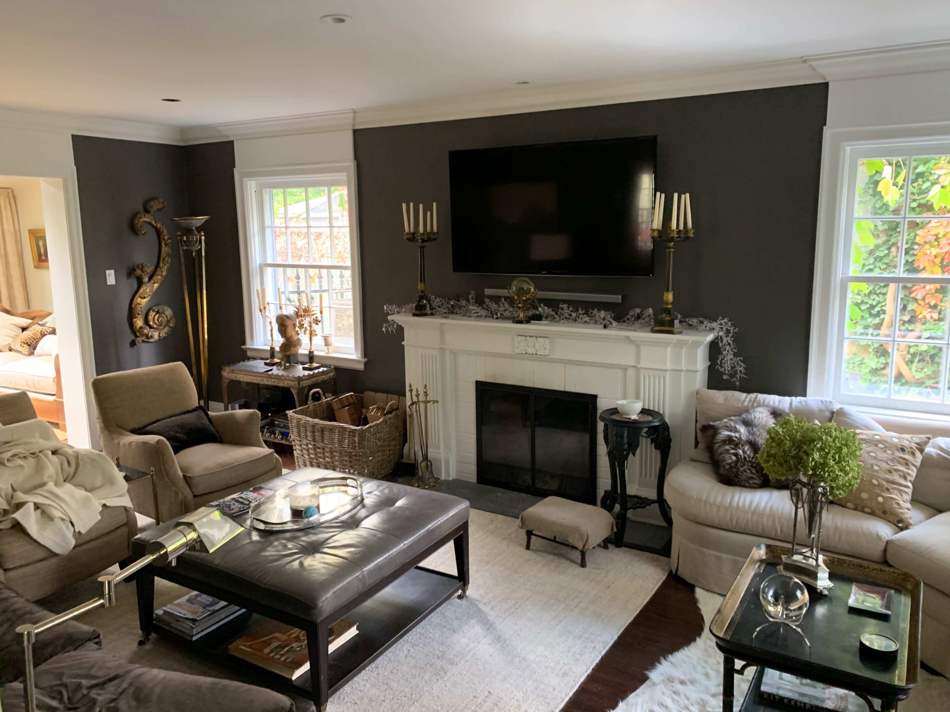 The living room features a dark accent wall, a large flat-screen TV above a white fireplace, and beige seating arranged around a coffee table.