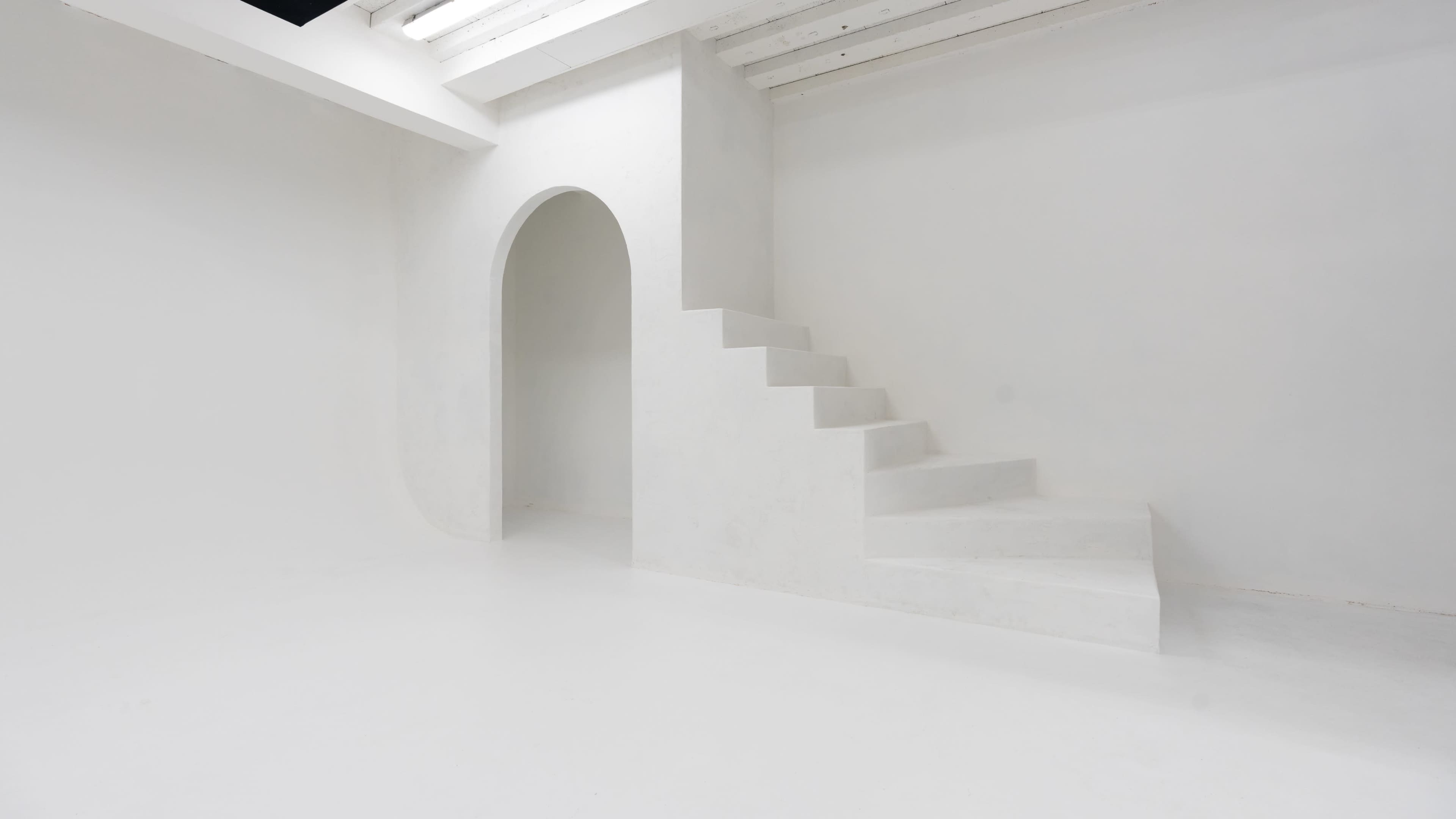 The image shows a minimalistic, all-white interior featuring a staircase leading up to an archway.