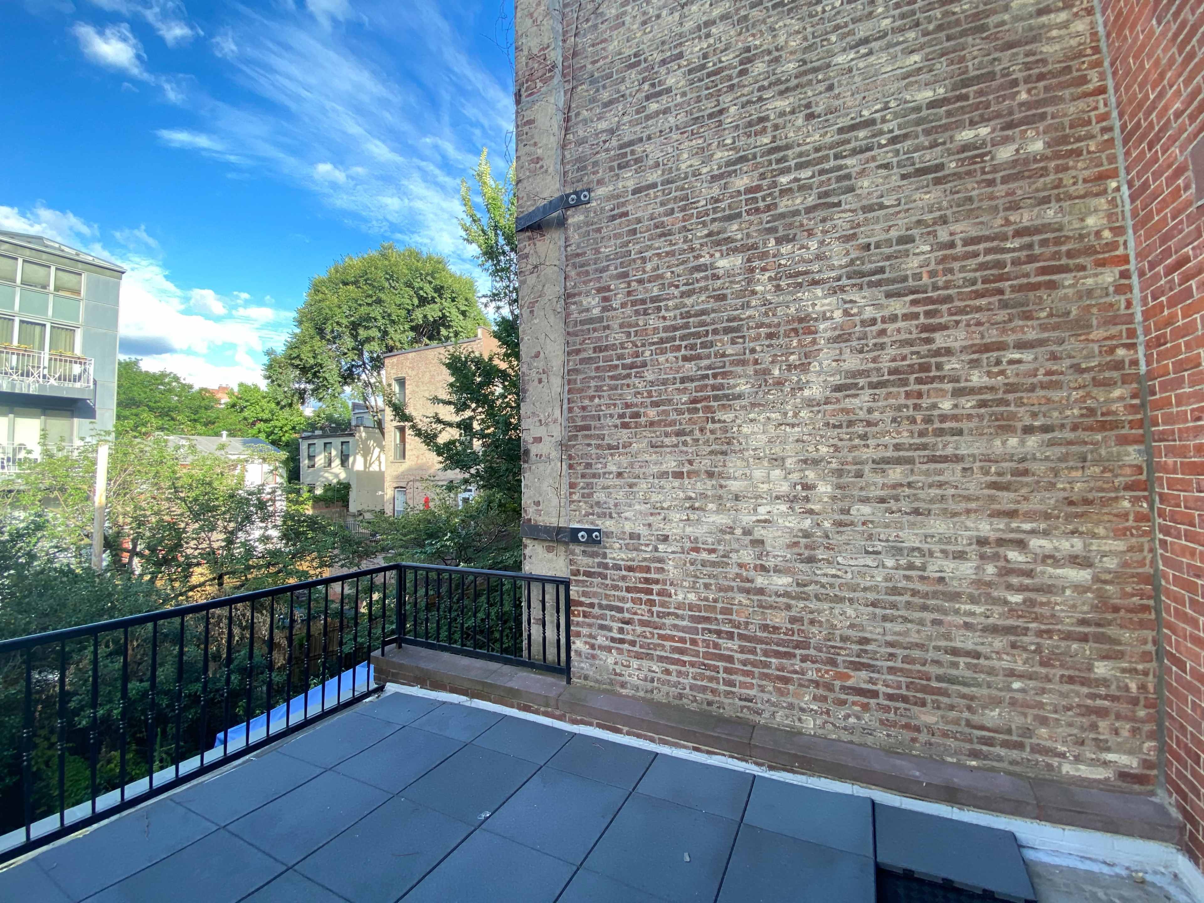 A rooftop terrace with a view of a brick wall and nearby buildings under a blue sky.