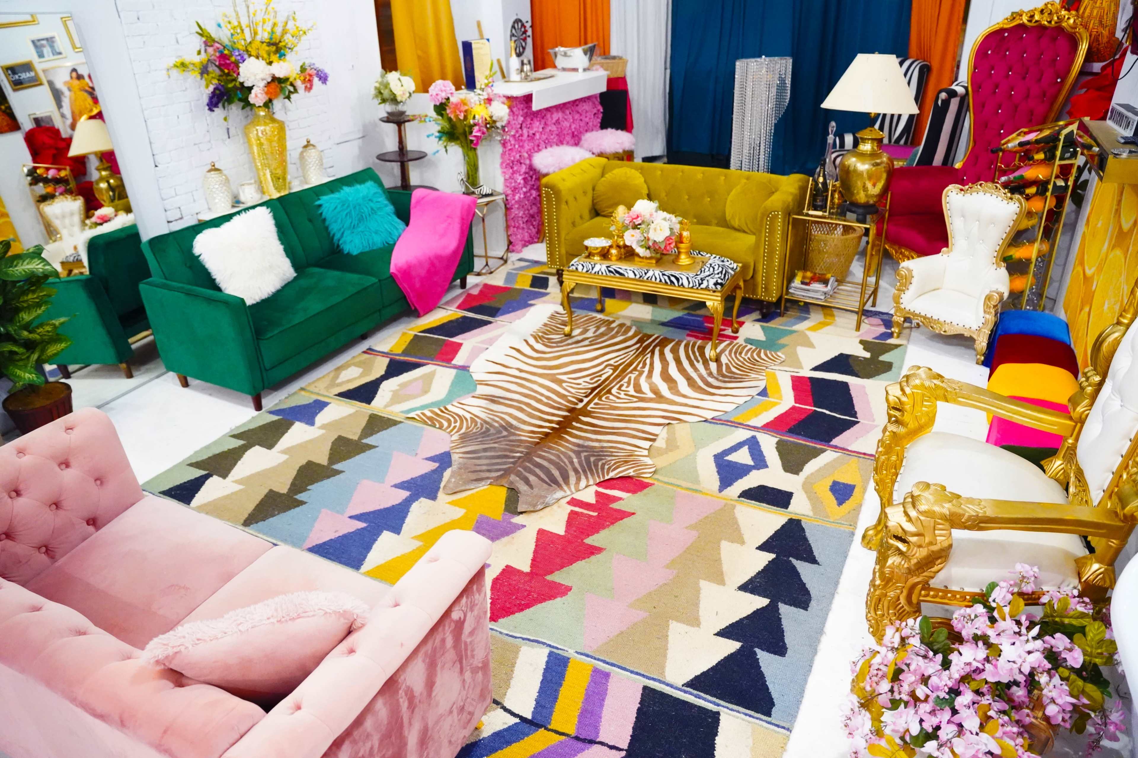 A vibrant lounge area with various colorful seating arrangements, including green and pink sofas, a patterned rug, and decorative floral arrangements.