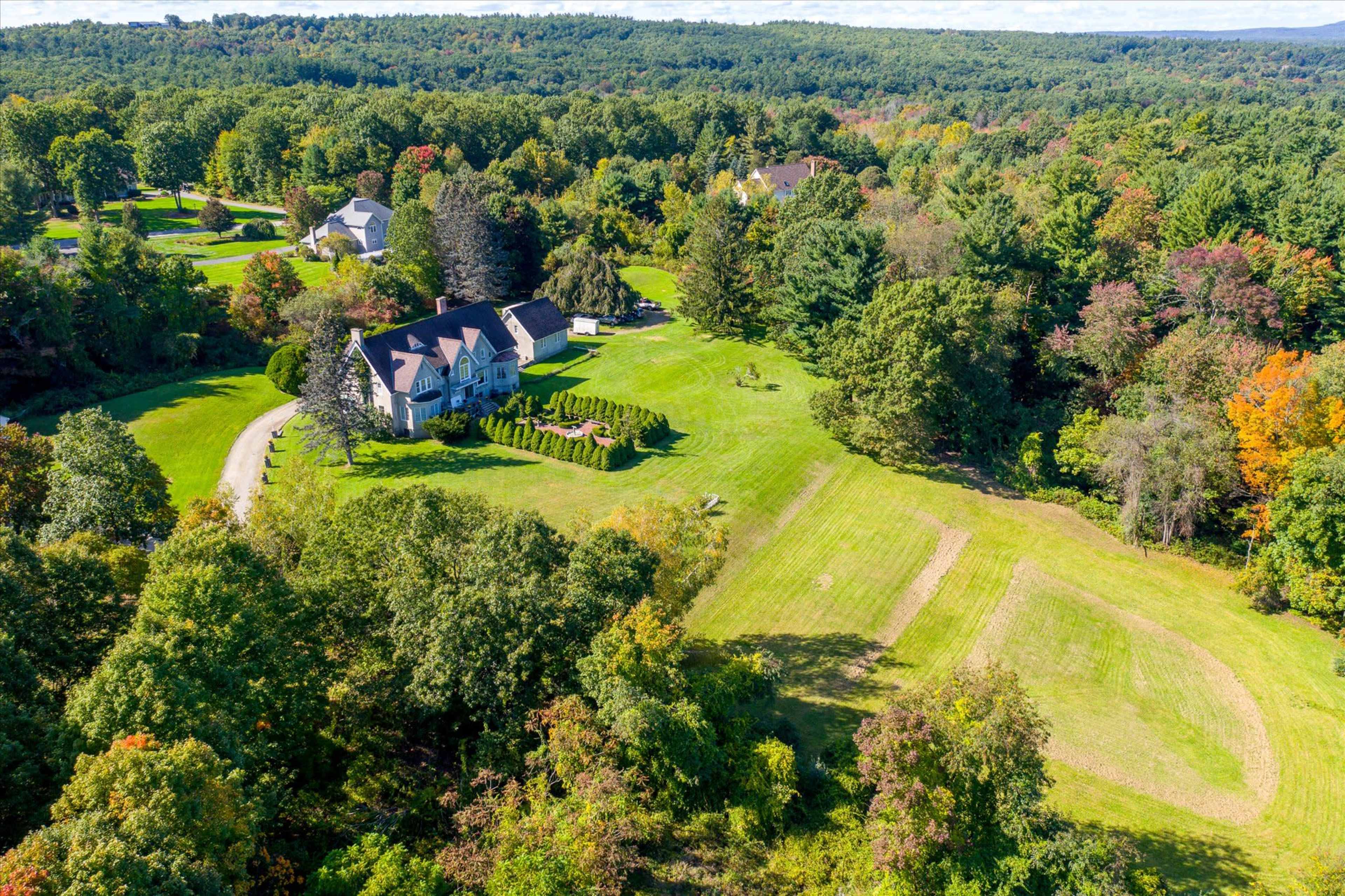 A large house with a landscaped yard is surrounded by trees and fields, set in a rural area with rolling hills.