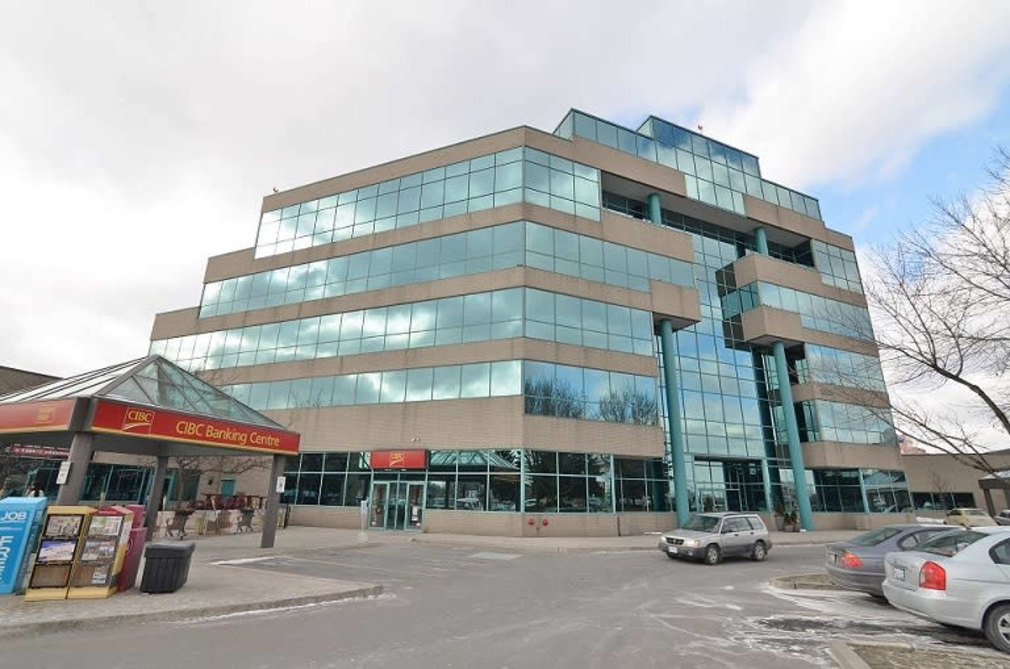 A modern bank building with a glass facade is situated next to a covered entrance marked "CIBC Banking Centre."