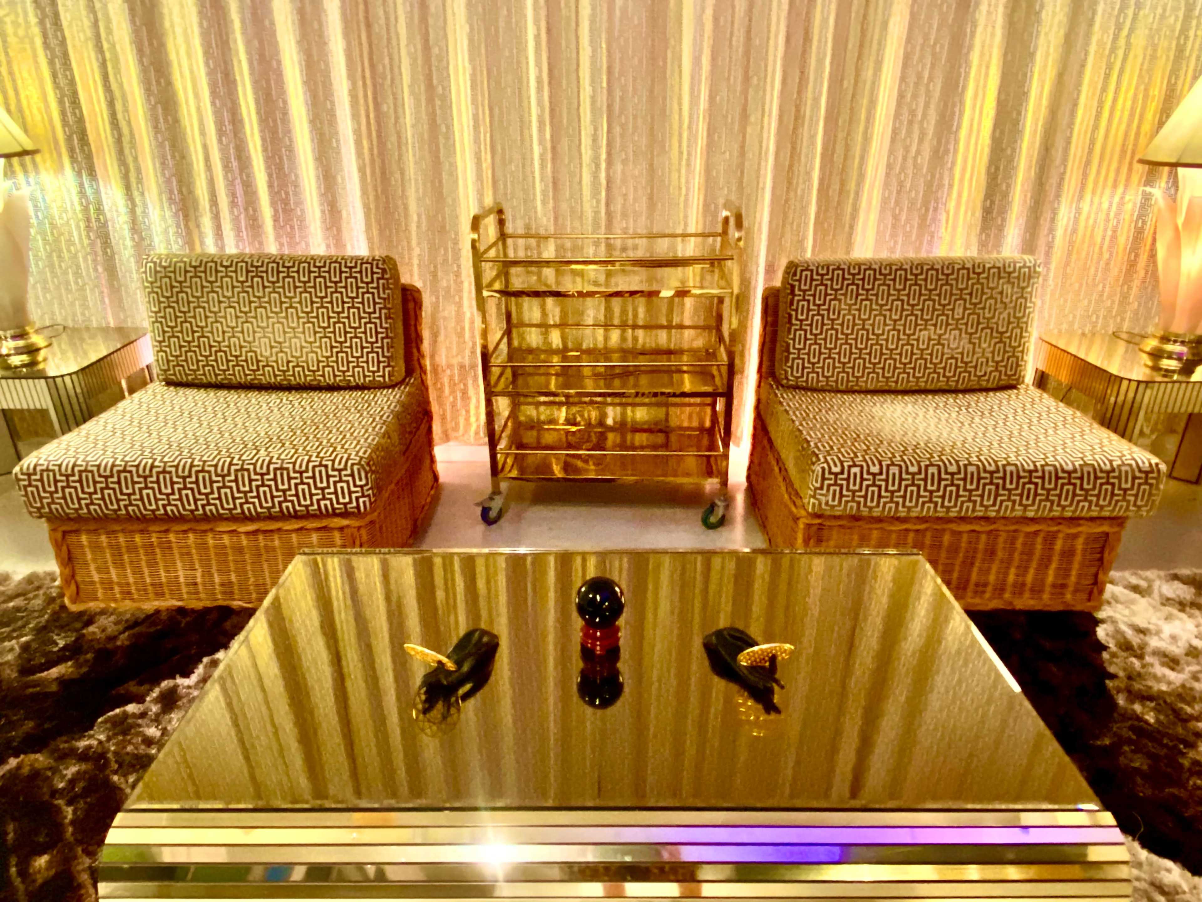 The image features two patterned chairs facing a mirrored coffee table, with a folding rack and soft lighting in the background.