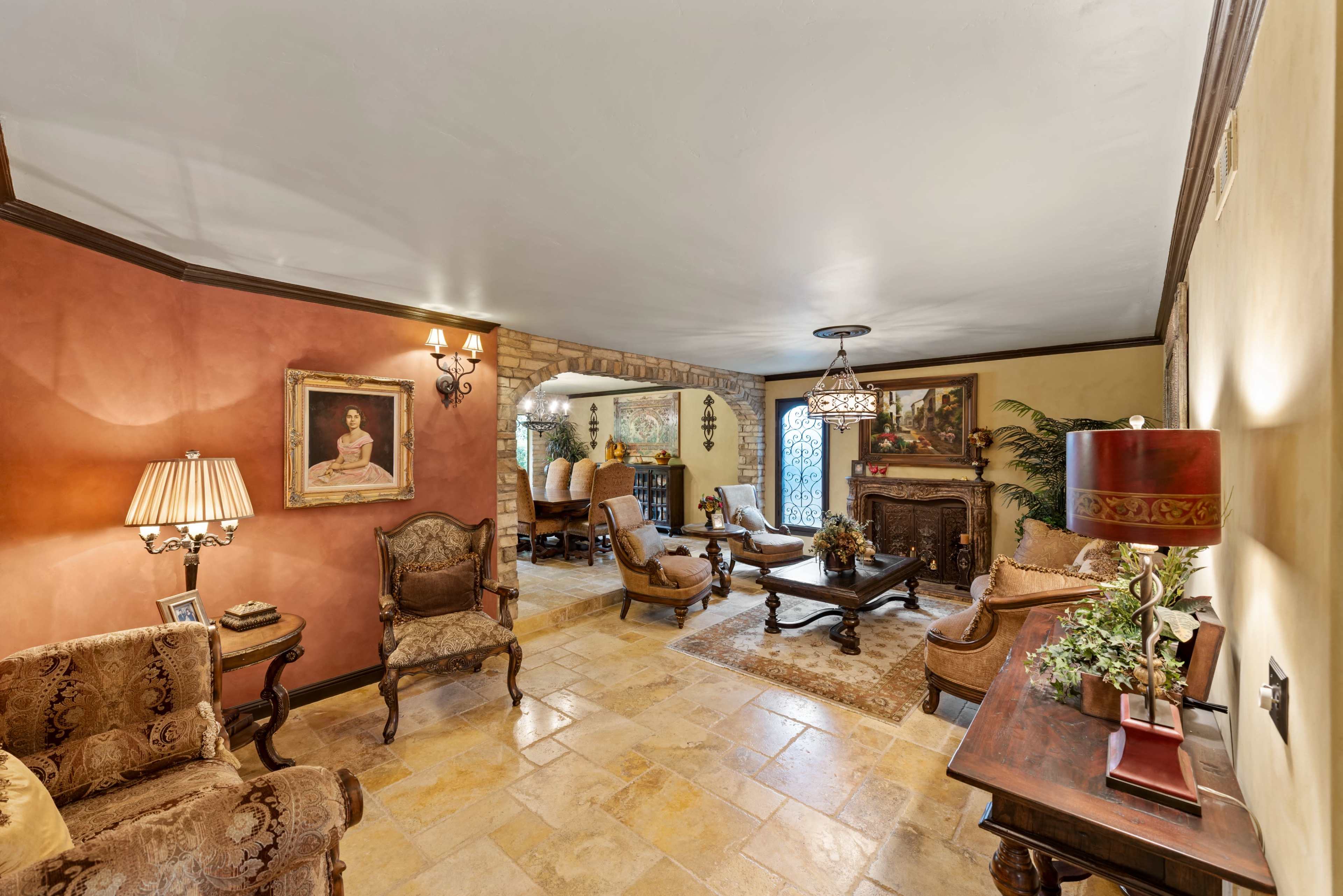 The image shows a living room with ornate furniture, a coffee table, and a decorative lamp, leading to an adjacent dining area with a lighted archway.