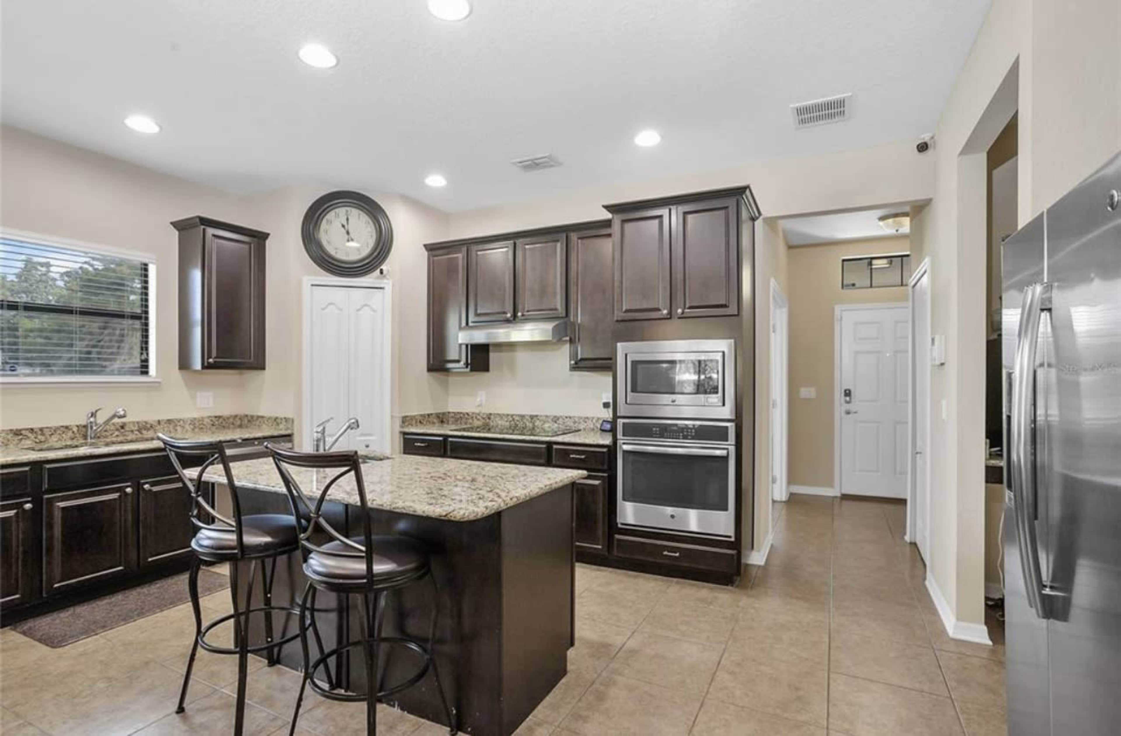 A modern kitchen with dark wooden cabinets, granite countertops, and stainless steel appliances, including an oven and refrigerator.