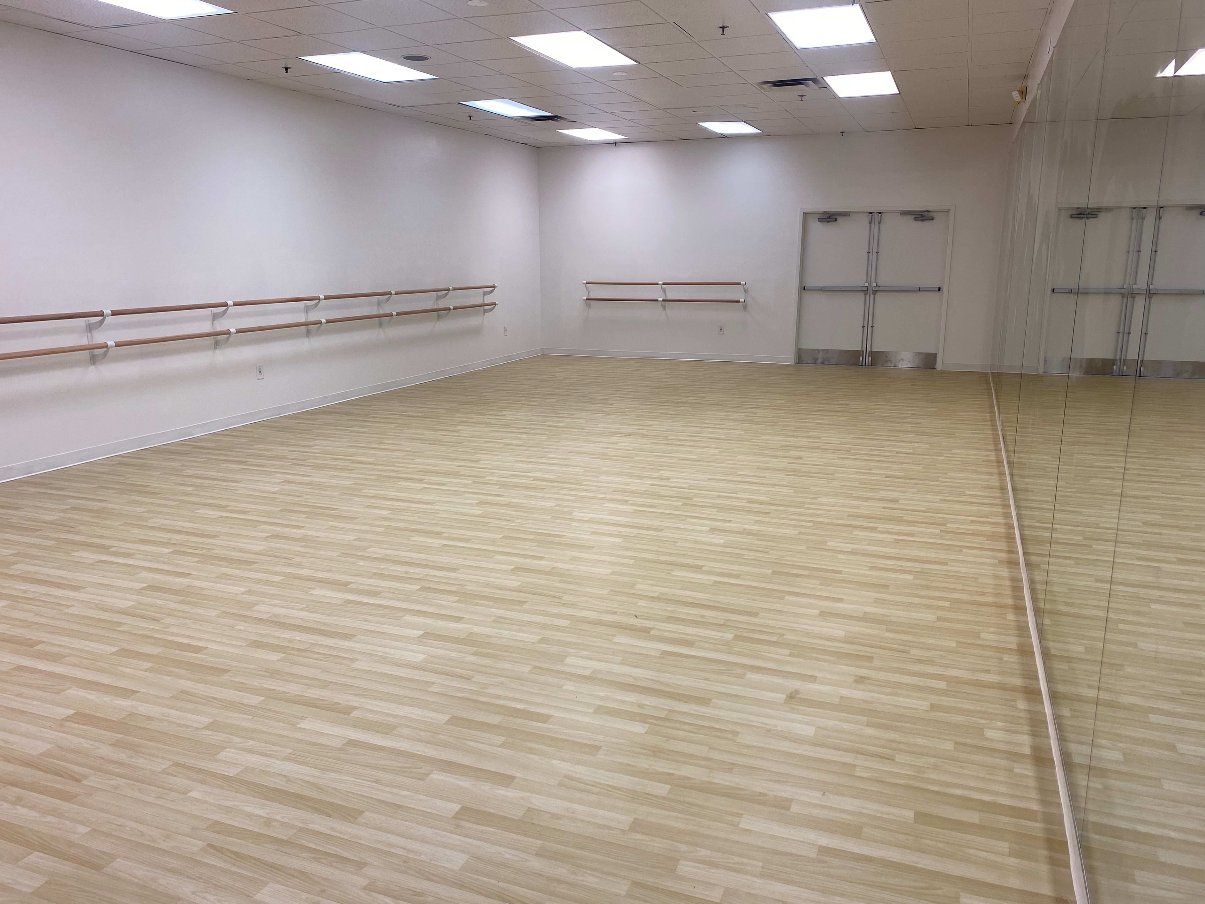 A dance studio with wooden flooring, mirrored walls, and barre installations along one side.
