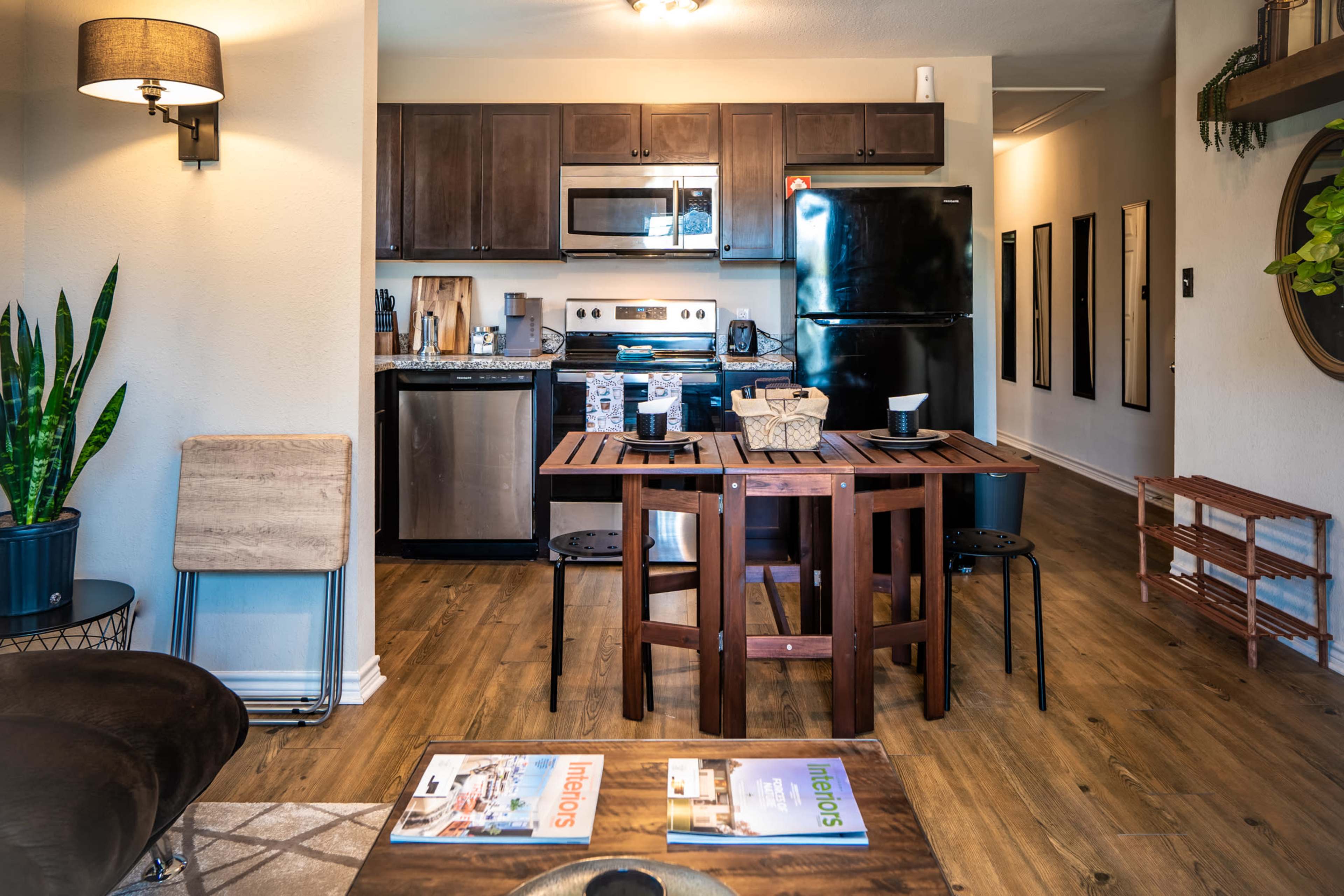 A modern kitchen and dining area features brown cabinetry, stainless steel appliances, and a small table set for two.