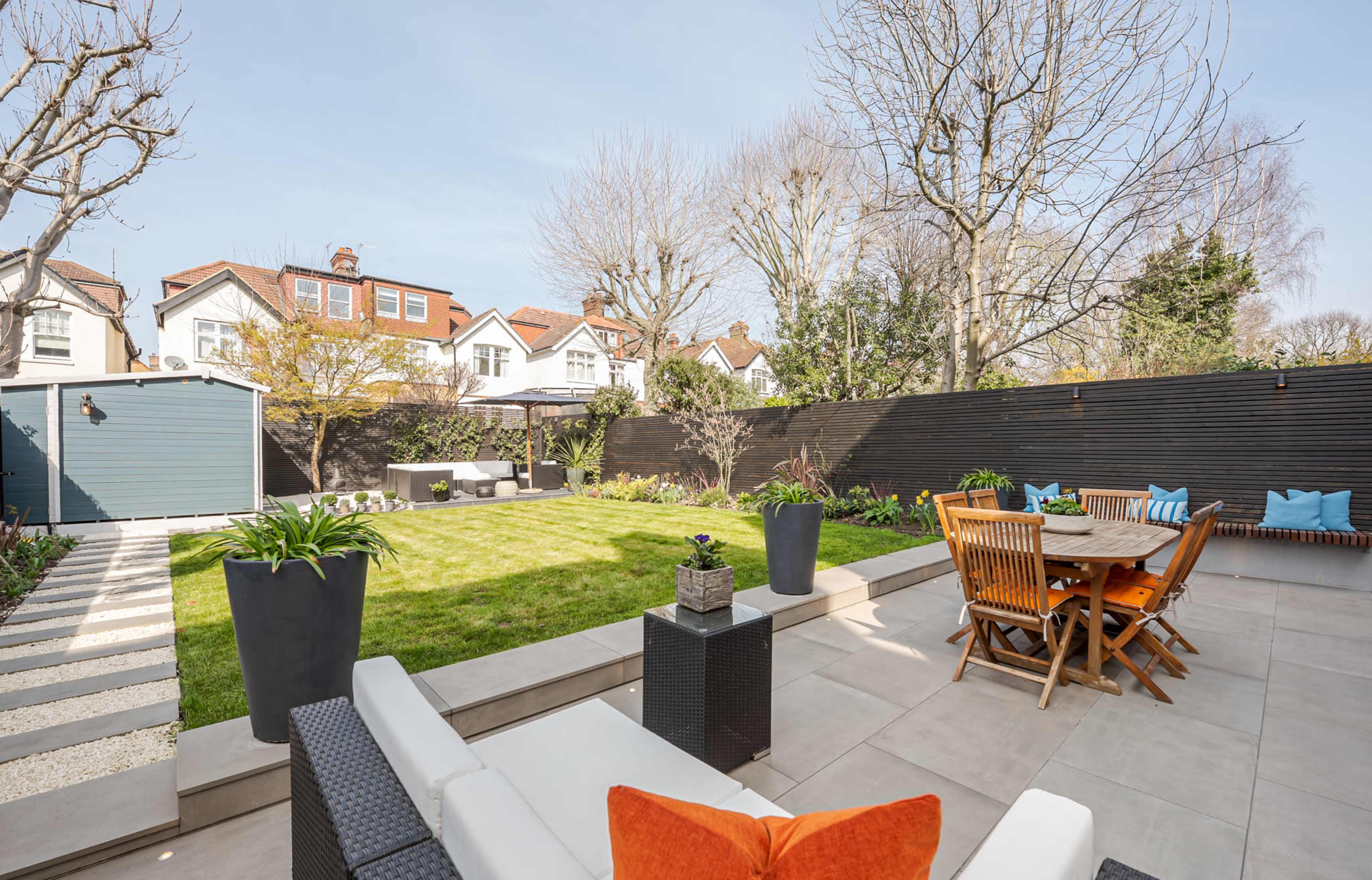 A landscaped backyard features a neatly maintained lawn, patio seating, and a dining area surrounded by trees and shrubbery.
