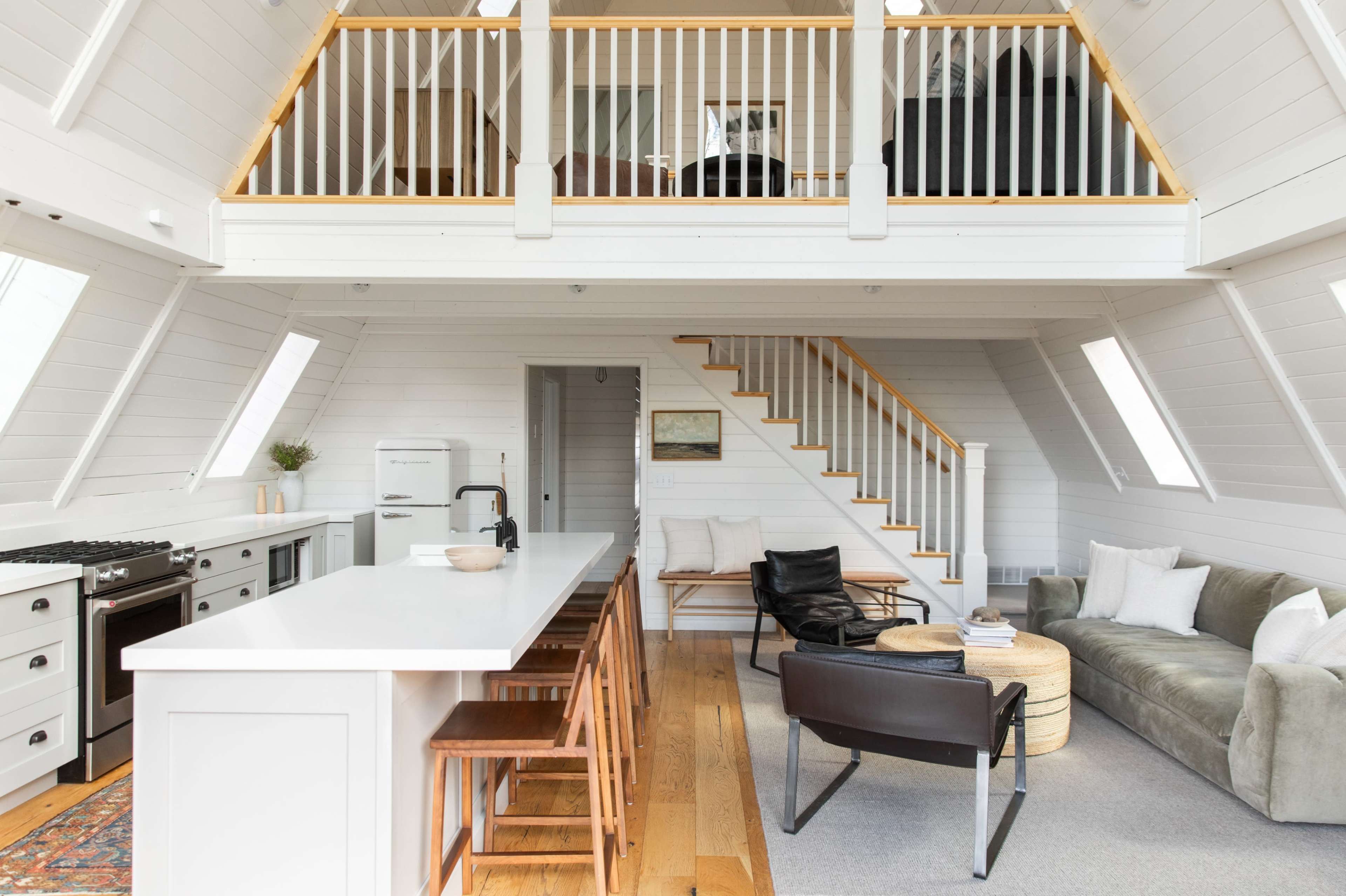 The interior of a modern, open-plan living space features a kitchen with a long island, a cozy seating area, and a staircase leading to a lofted area.