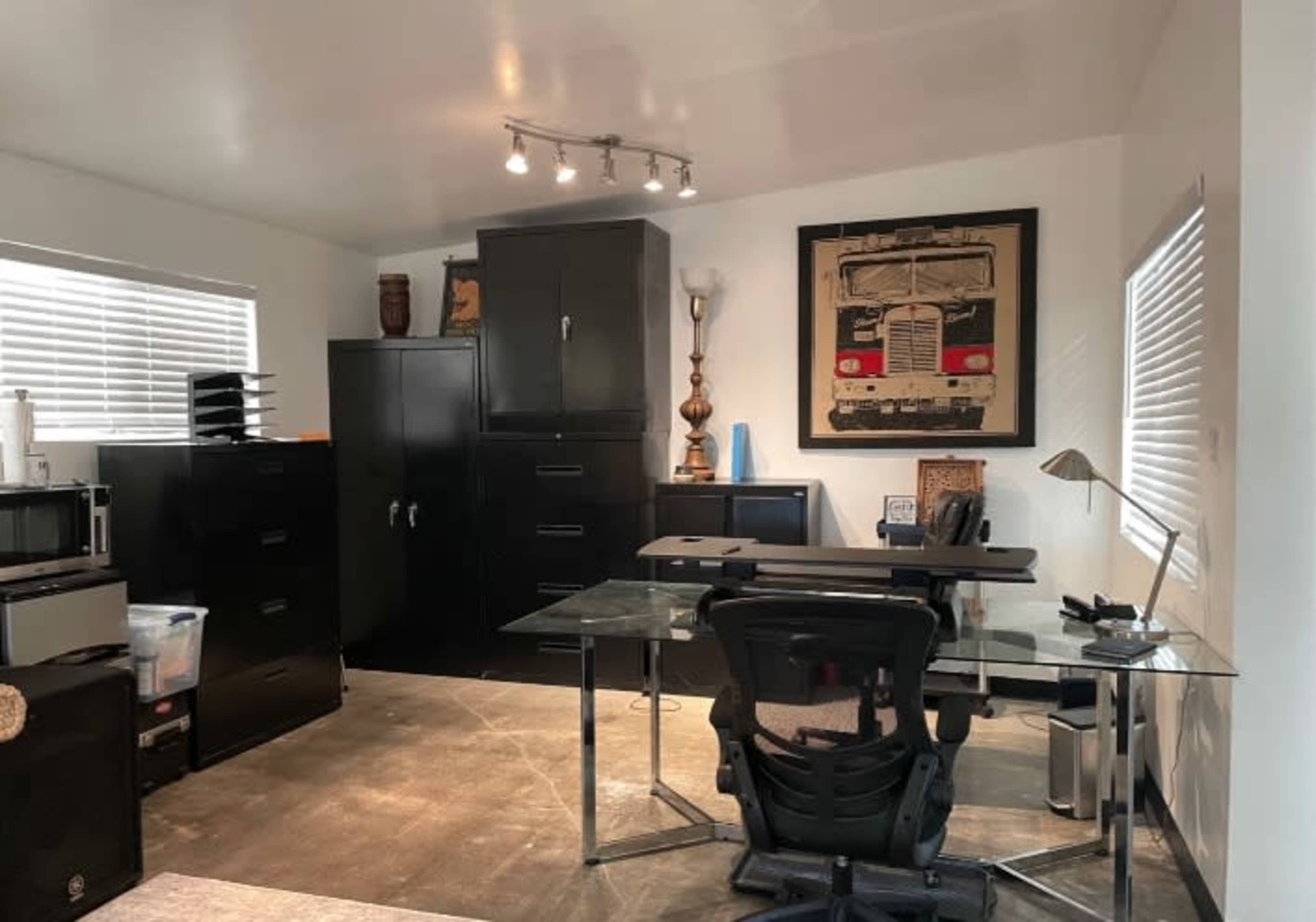 A modern office space features a glass desk, black filing cabinets, and a framed artwork on the wall.
