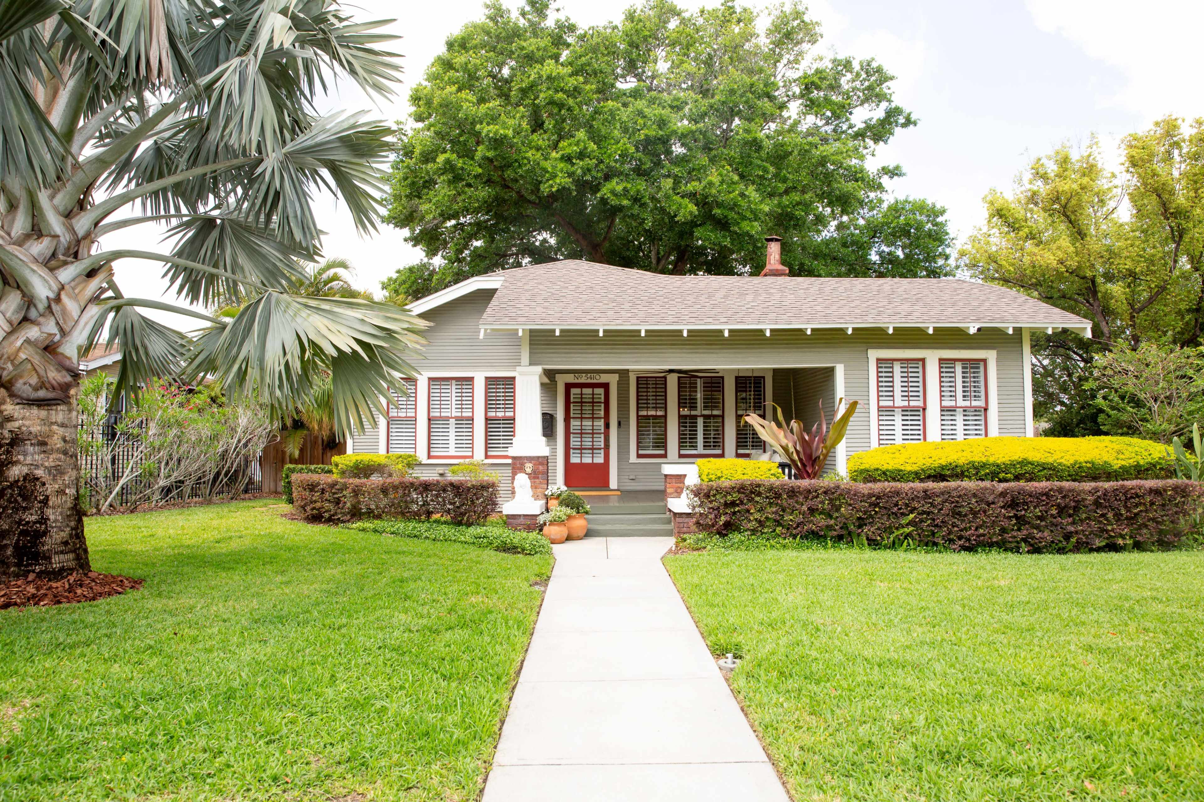A single-story house with a front porch is surrounded by greenery and a neatly maintained lawn.