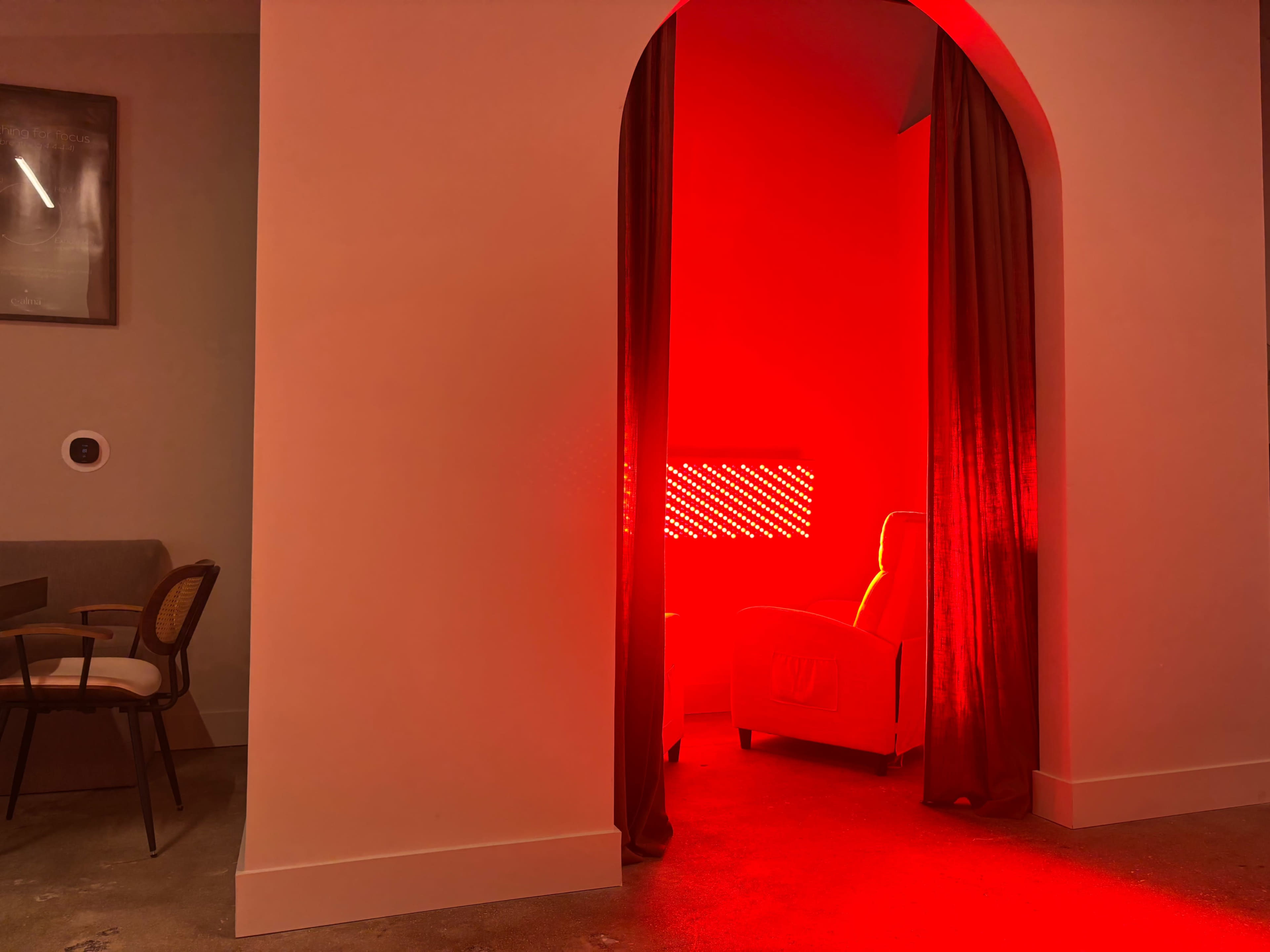 A vibrant red light fills a room through an archway, illuminating a chair in the corner.