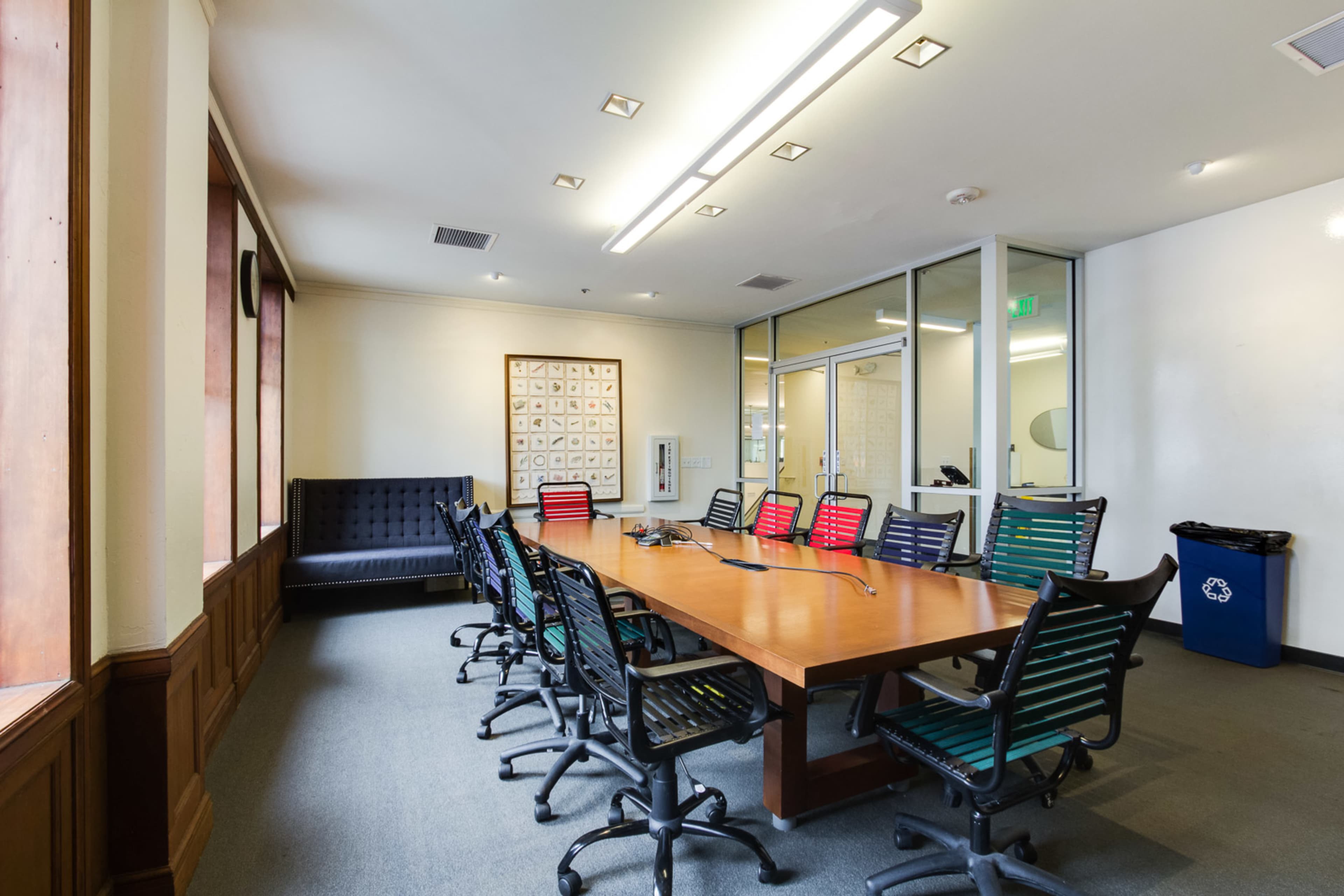 A conference room with a long wooden table surrounded by rolling office chairs and a large couch against one wall.