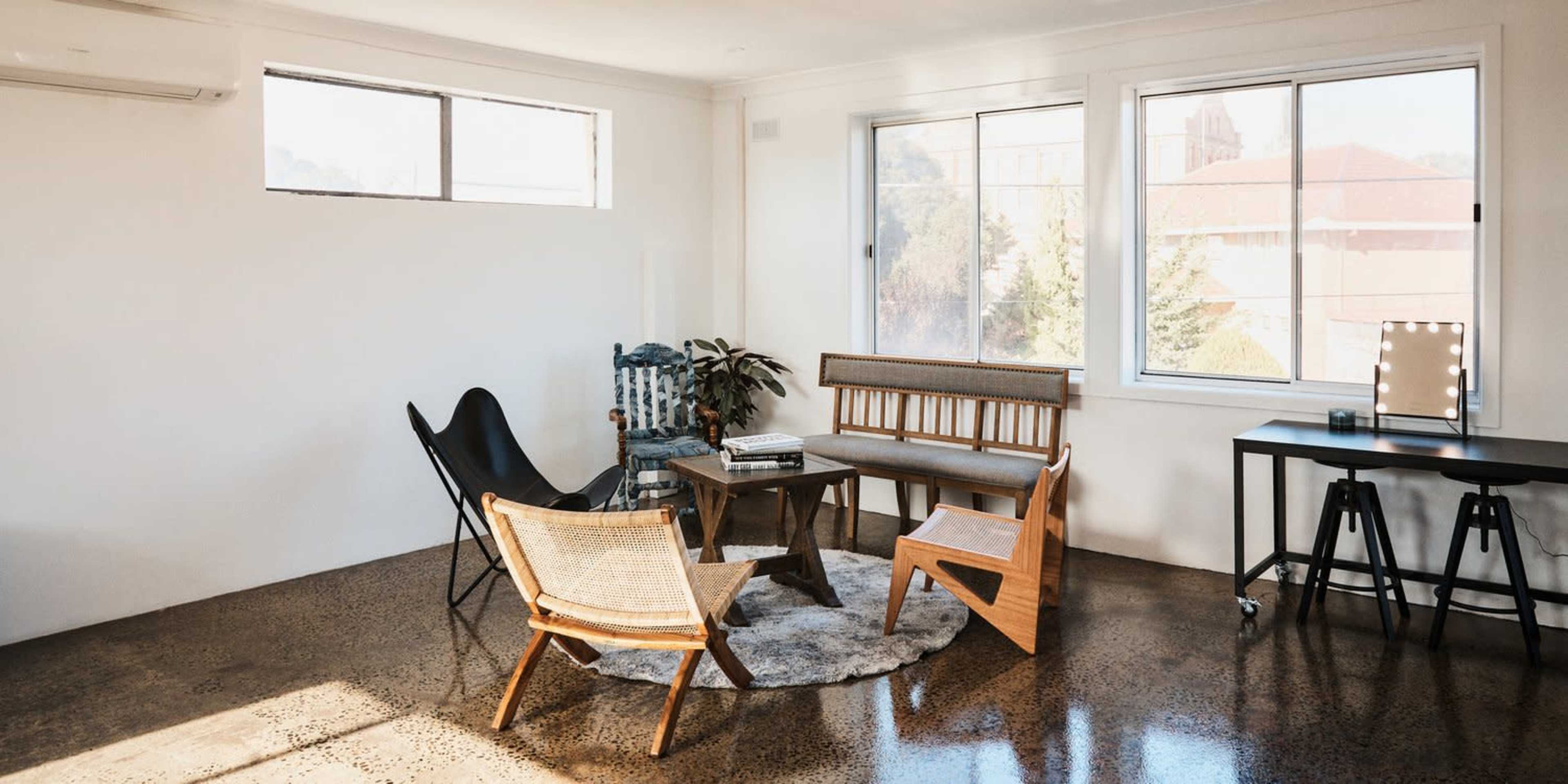 A contemporary living room with a few pieces of furniture, including a wooden bench, a butterfly chair, and a round rug, set against a backdrop of large windows.