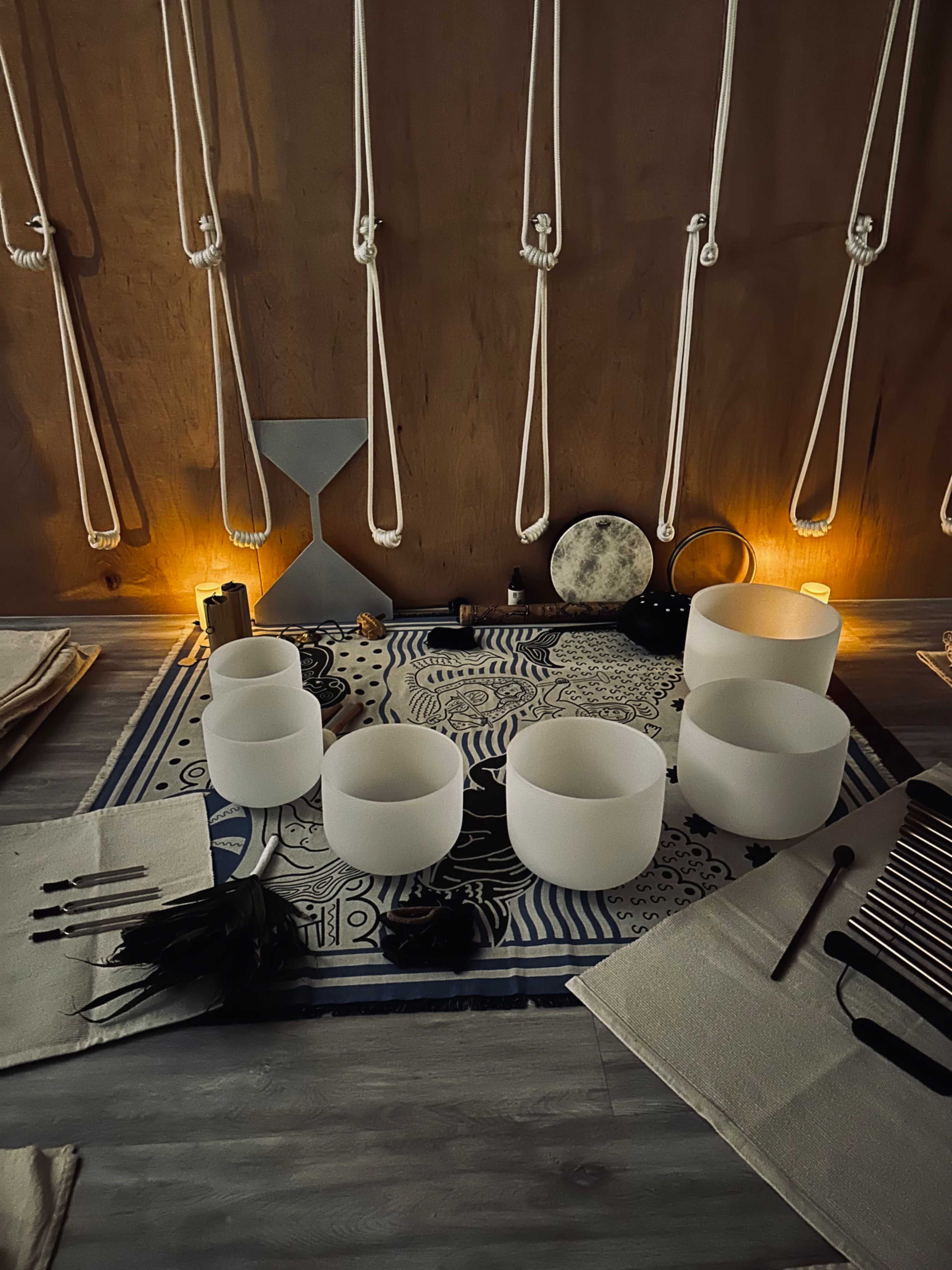 The image shows a dimly lit space arranged with various musical instruments, including crystal bowls and percussion tools, placed on a patterned mat.