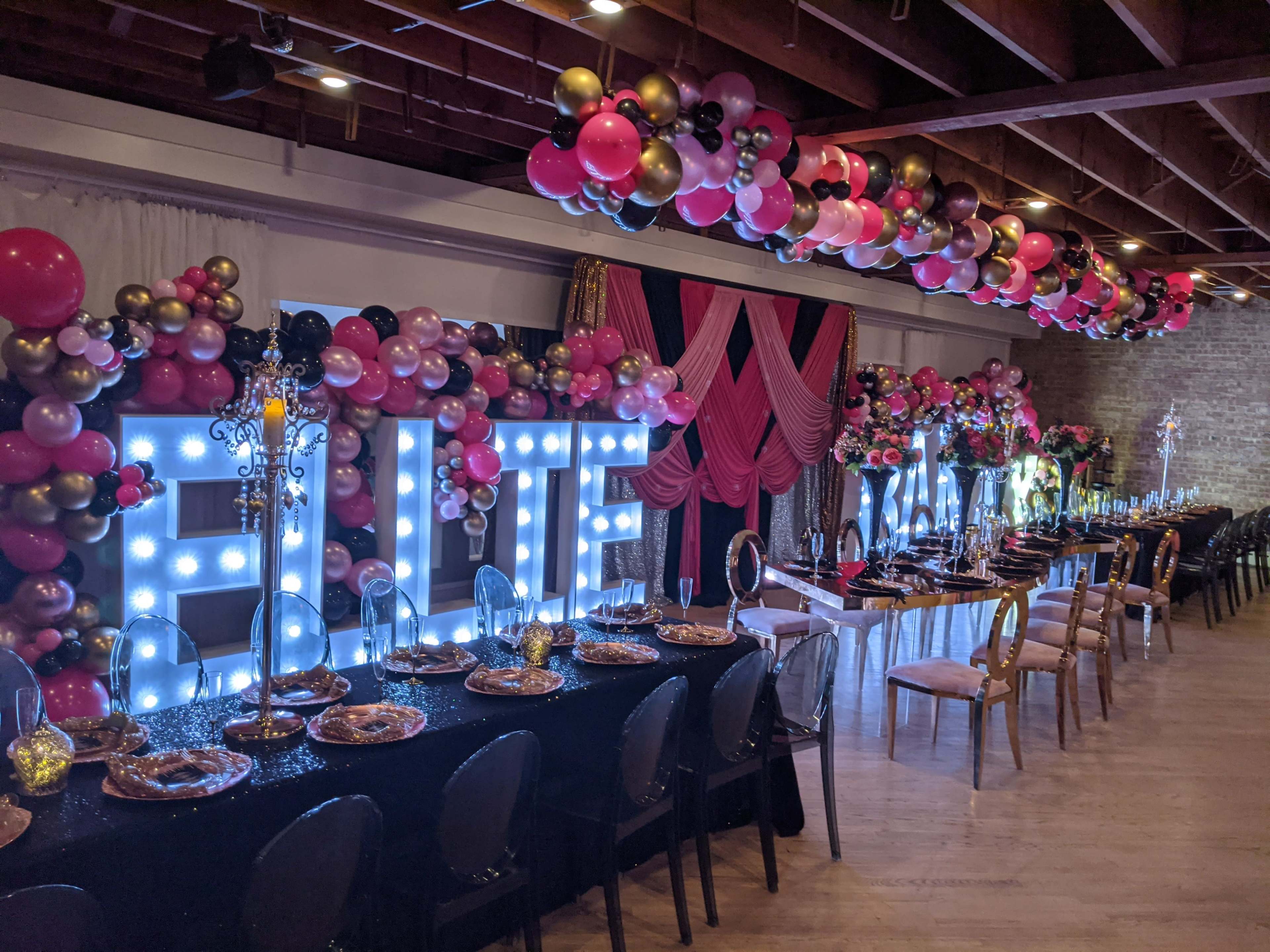 A decorated event space featuring large illuminated letters spelling "BLUE" and an elegantly set table adorned with balloons and stylish decor.