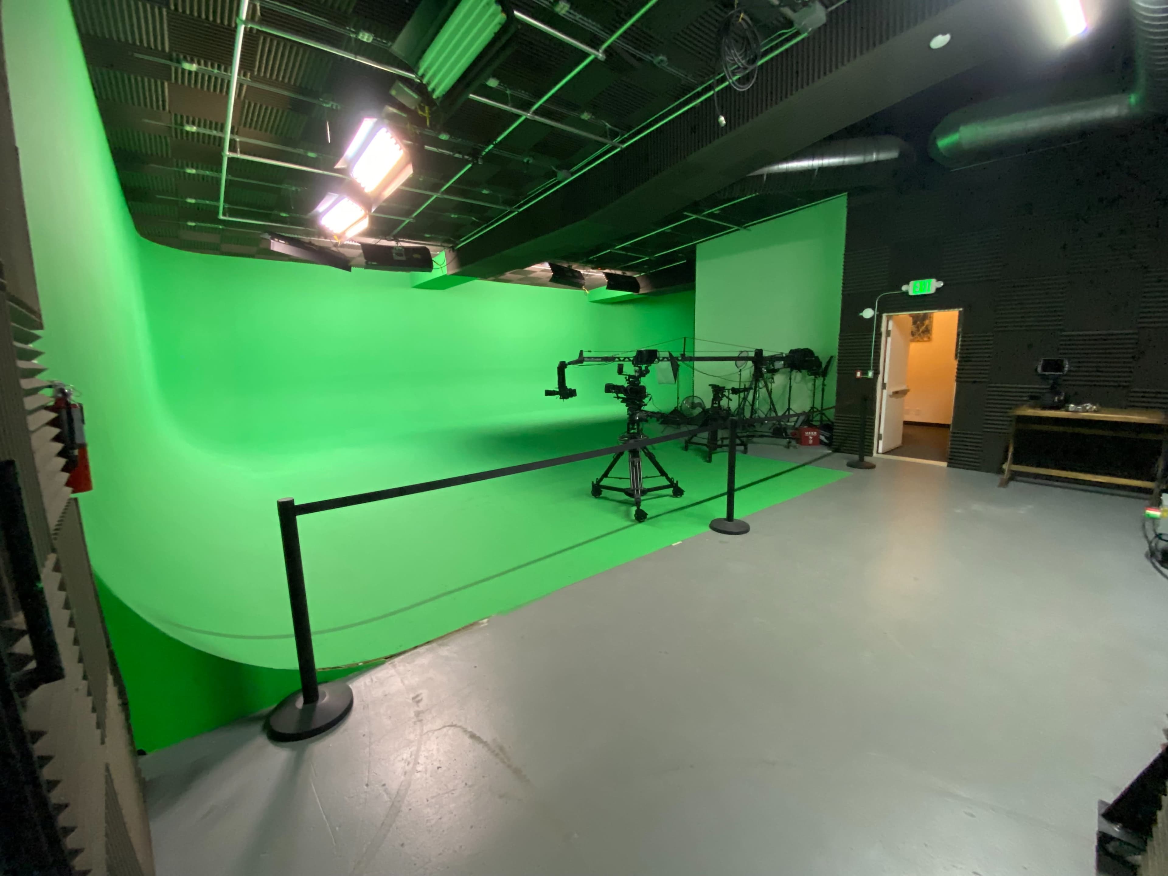 A green screen studio equipped with a camera on a tripod and various lighting setups.