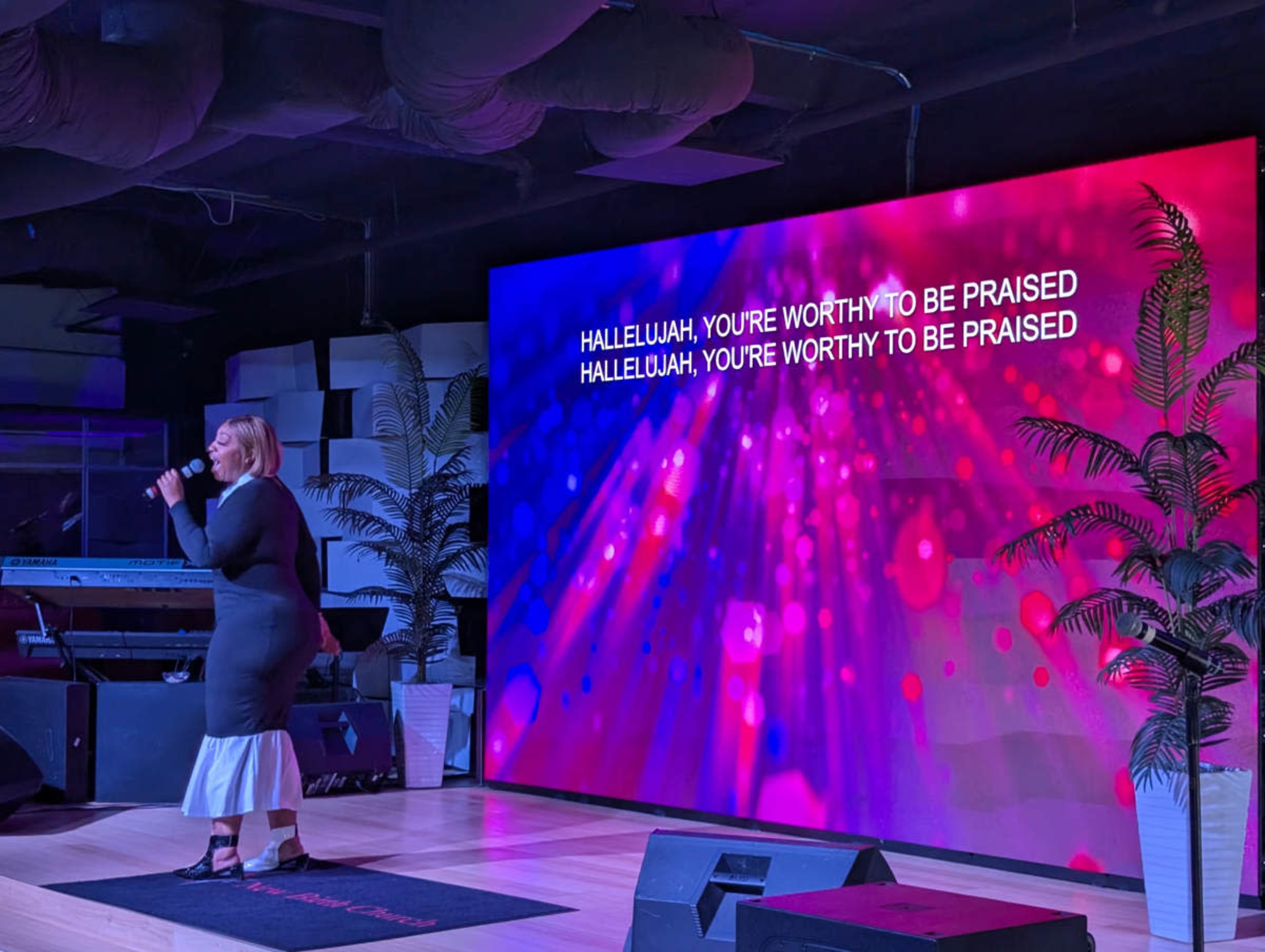 A singer performs on stage in front of a large screen displaying colorful text with lyrics.