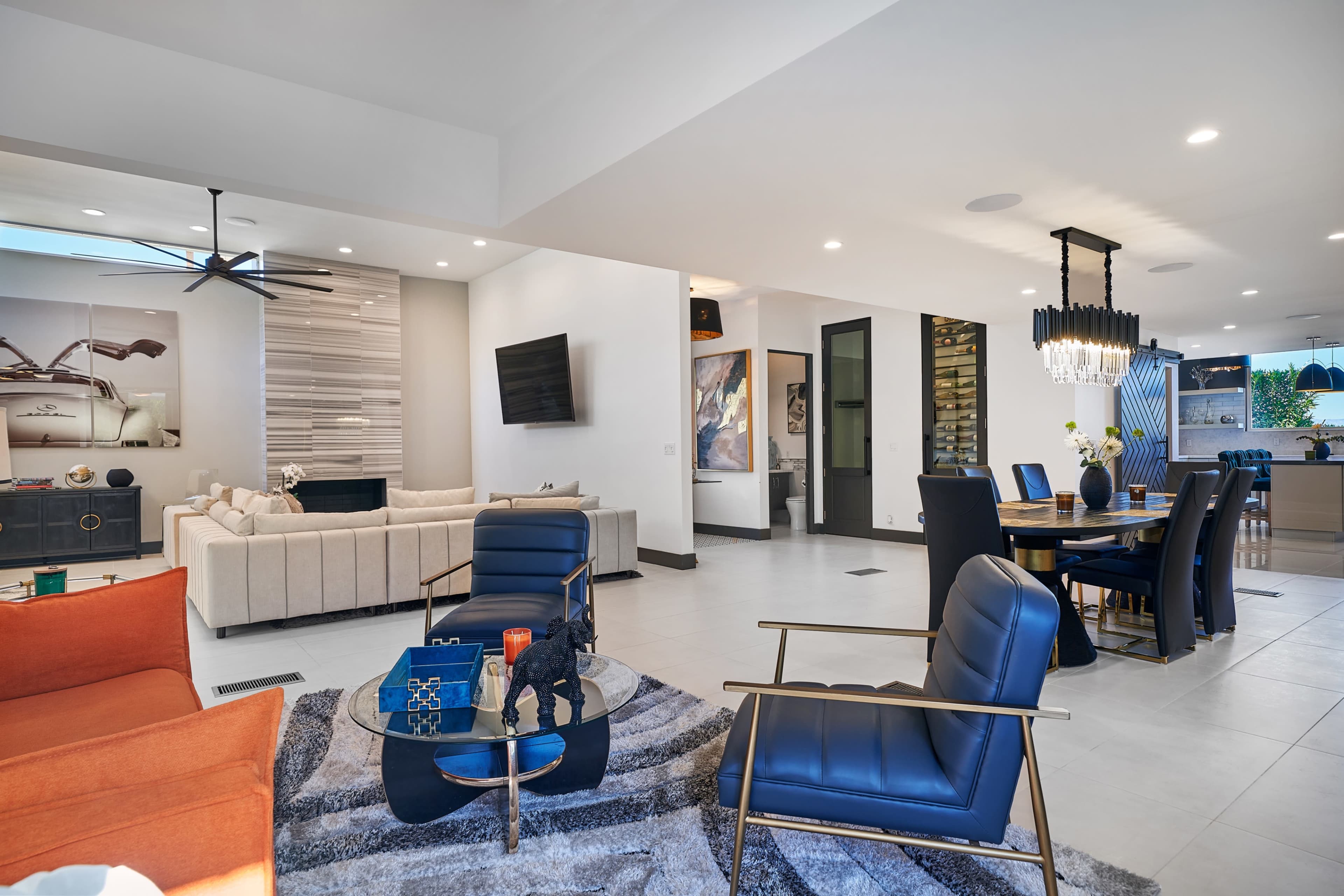 A modern living space featuring a seating area with orange and blue chairs, a gray rug, and a dining area with a round table and black chairs.
