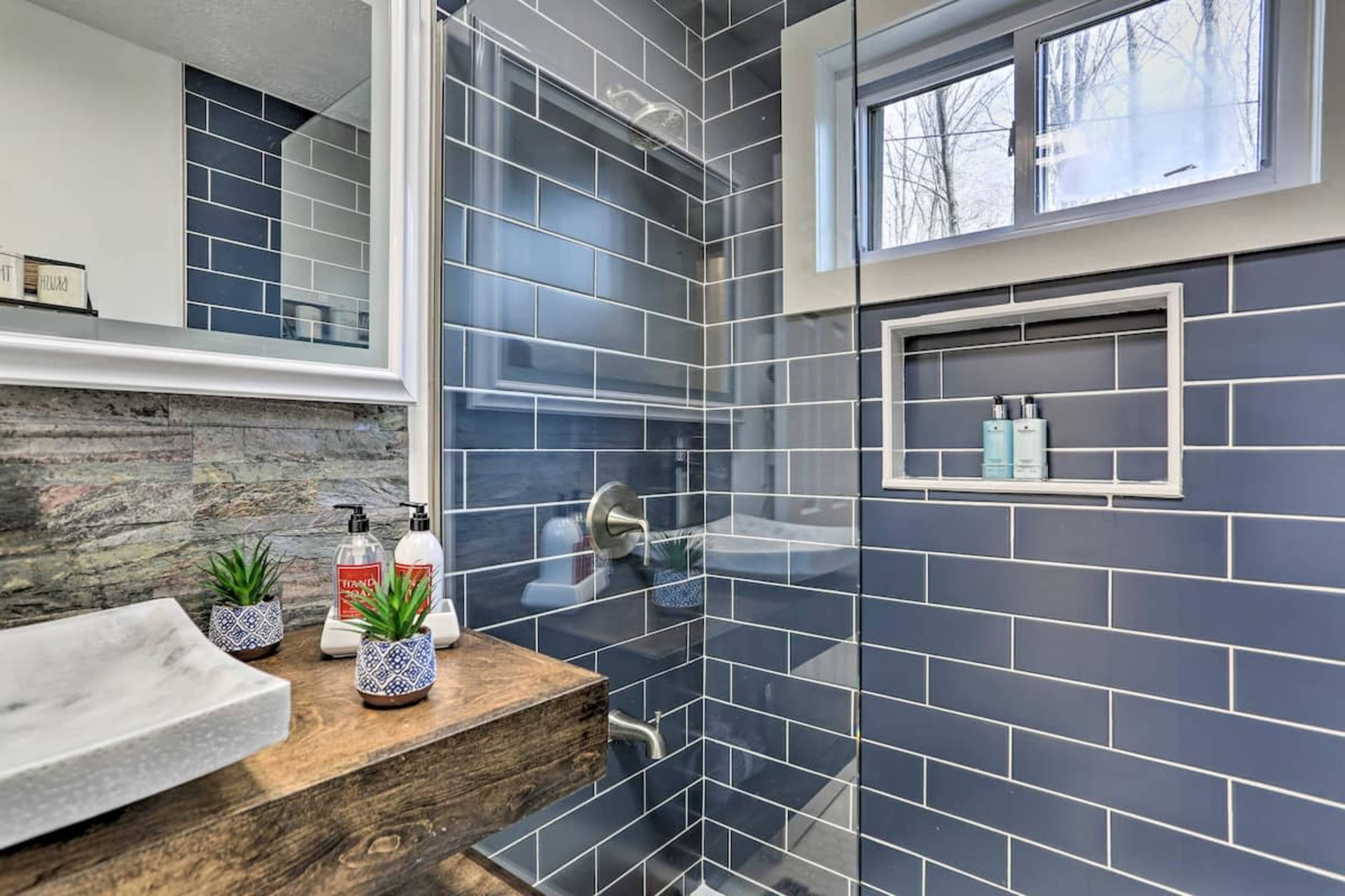 A modern bathroom with blue tiled walls, a glass shower enclosure, and a wooden vanity featuring decorative plants.