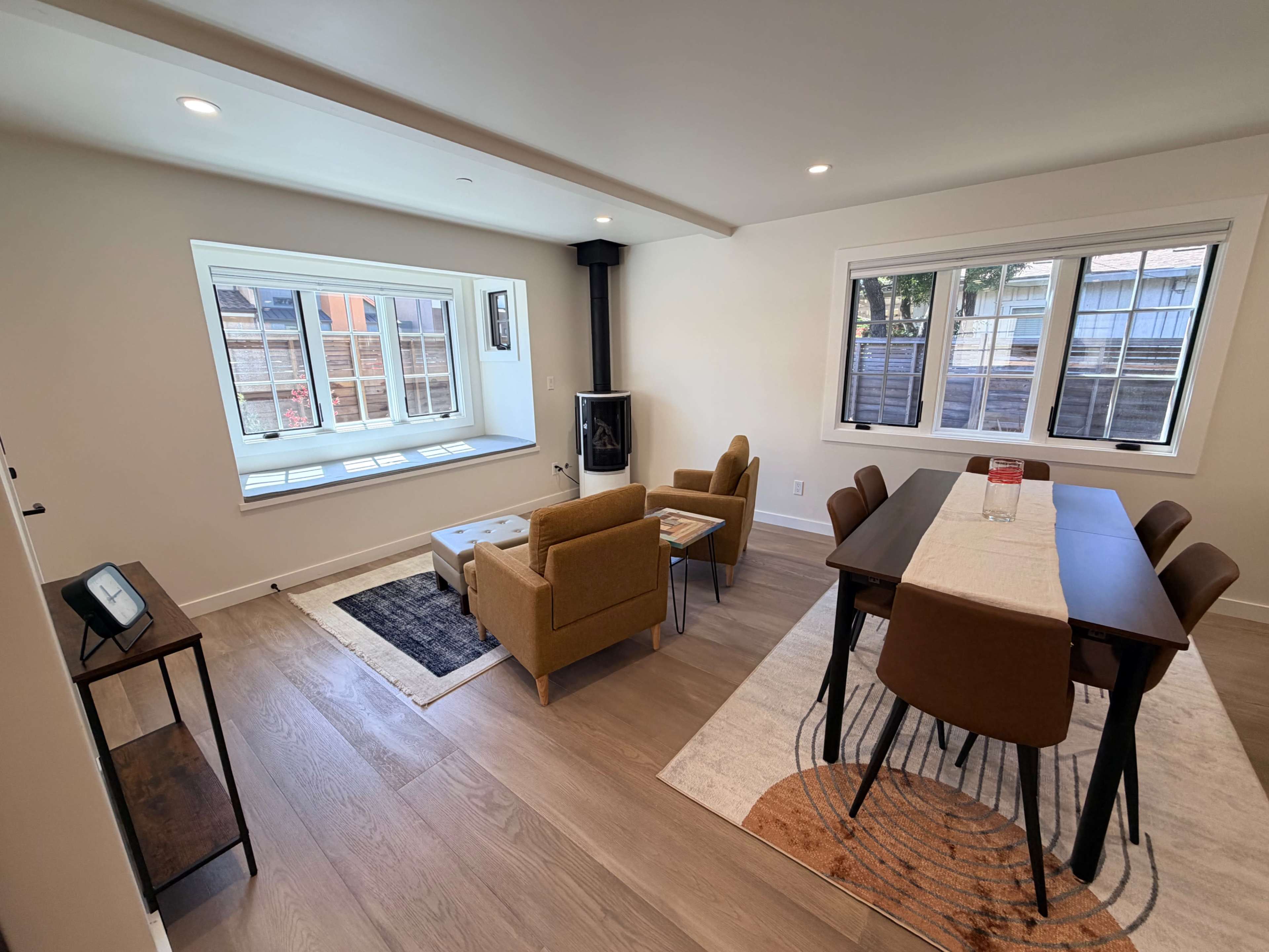 The image shows a modern living space featuring a seating area with two armchairs, a dining table with chairs, and a window allowing natural light in.