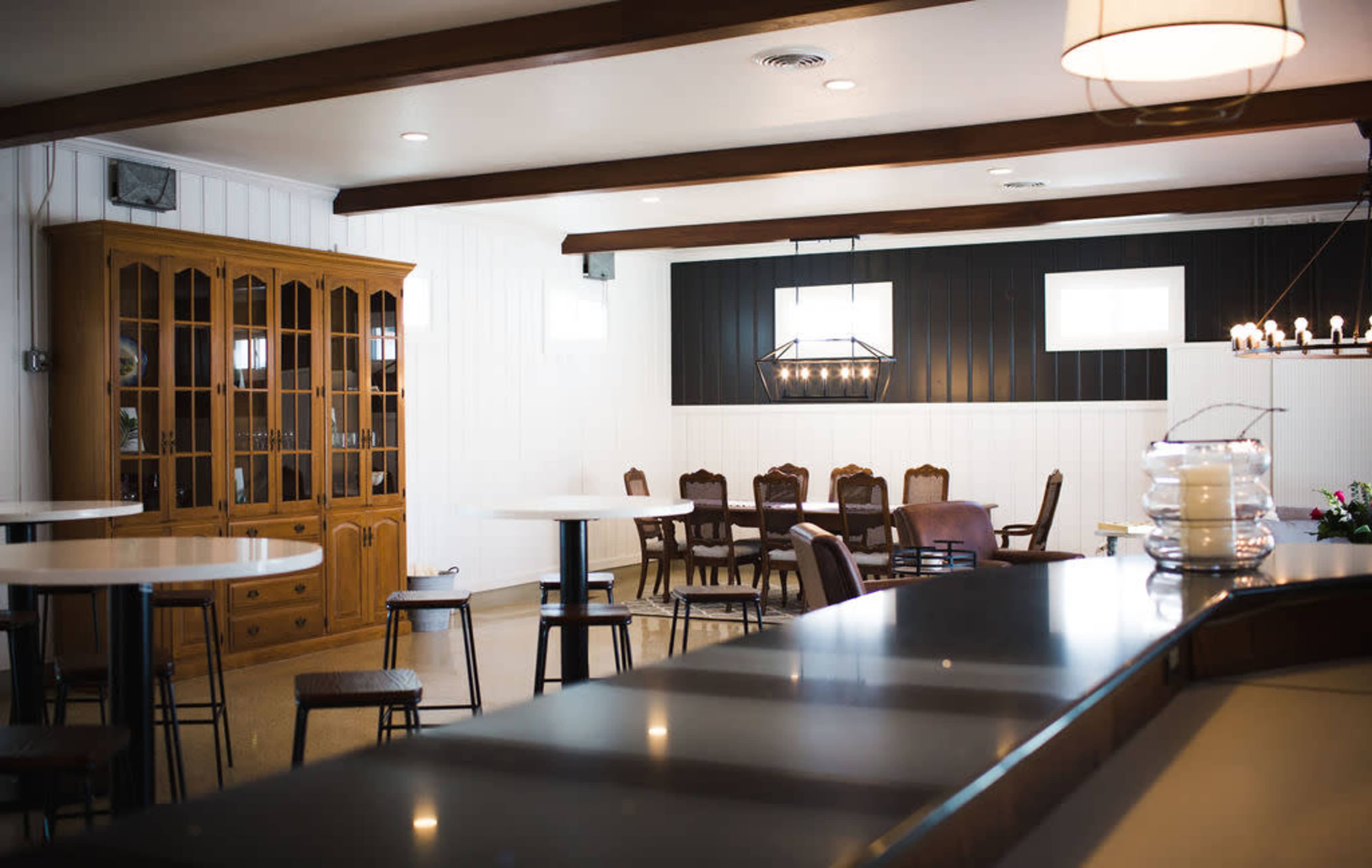 The image shows a modern dining area with a mix of table settings, wooden furniture, and a display cabinet against a backdrop of contrasting wall colors.