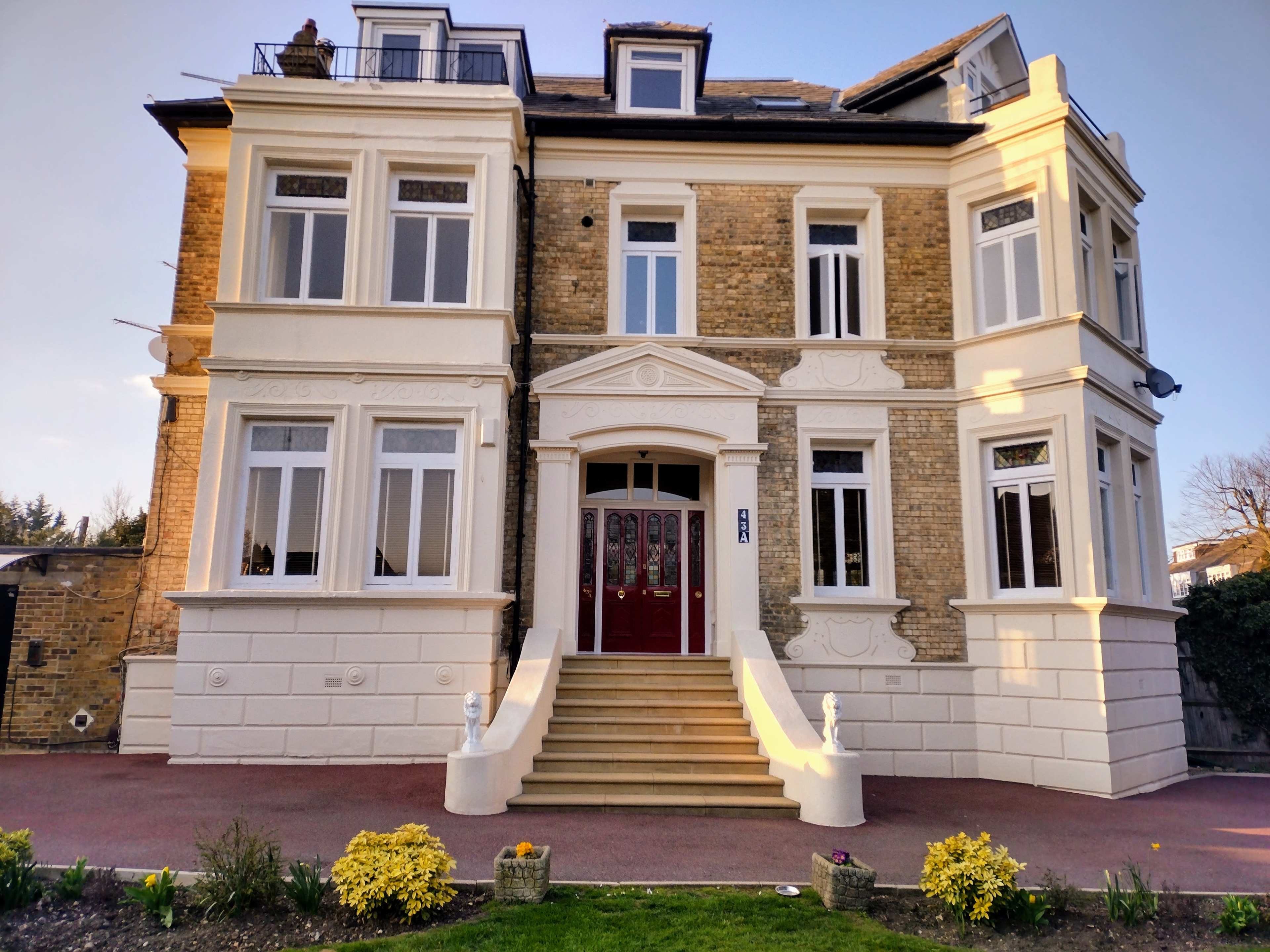 A large, three-story brick house with a white exterior, ornate detailing, and a red double door entrance.
