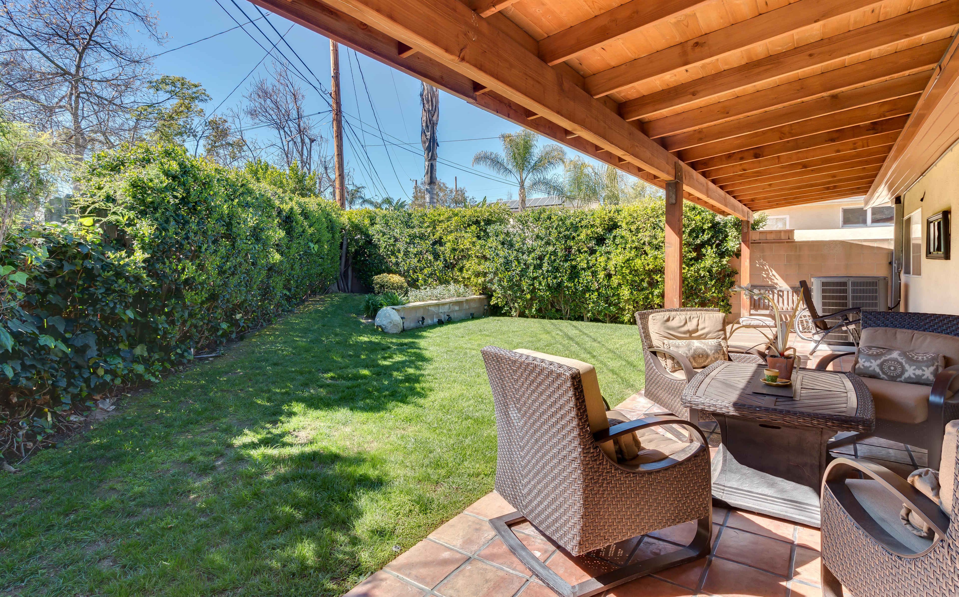 A patio area features outdoor seating and a landscaped garden with green grass and hedges under a wooden roof.