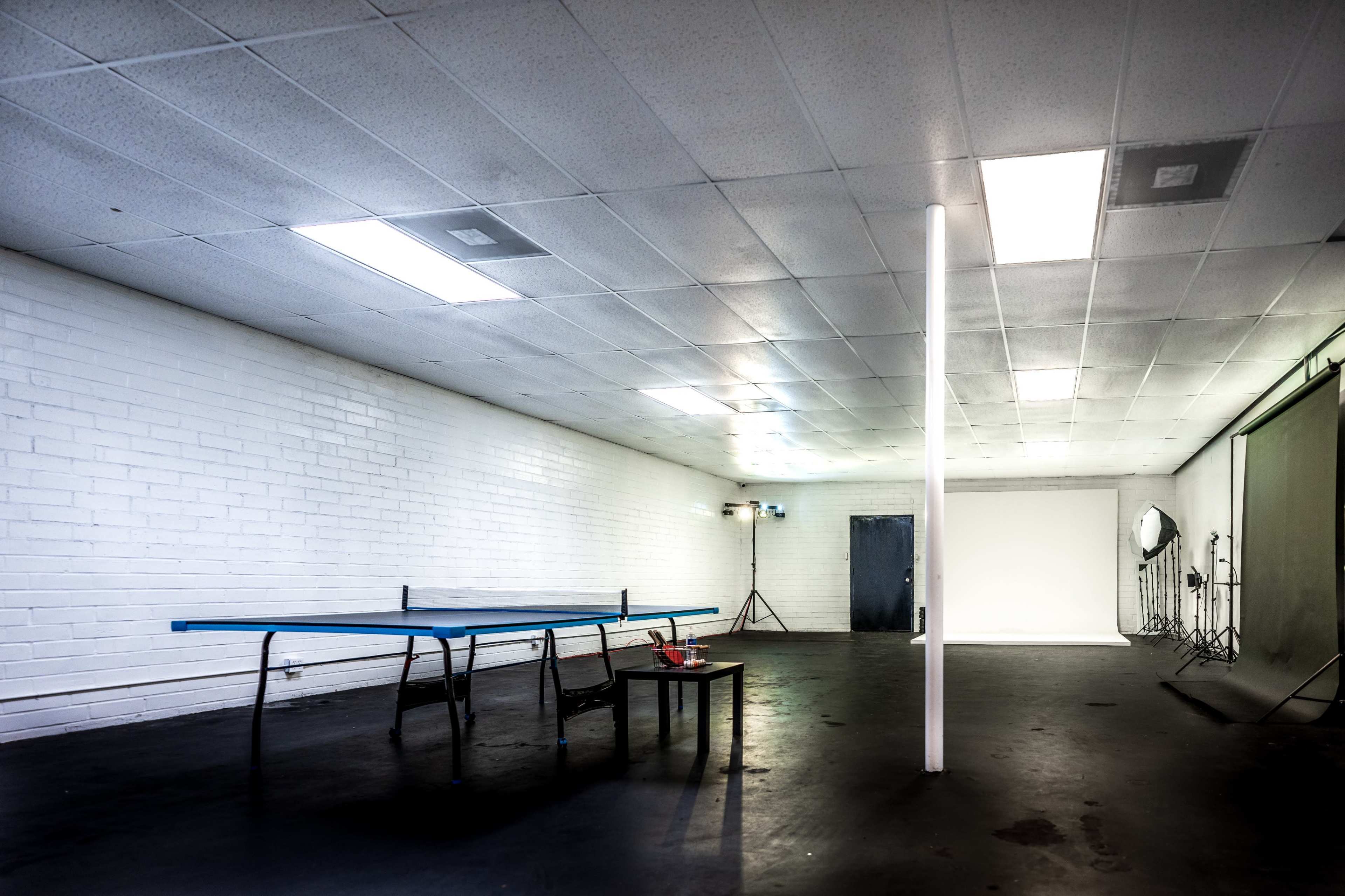 An empty room with a table, two chairs, and a partition dividing the space, illuminated by overhead lights.