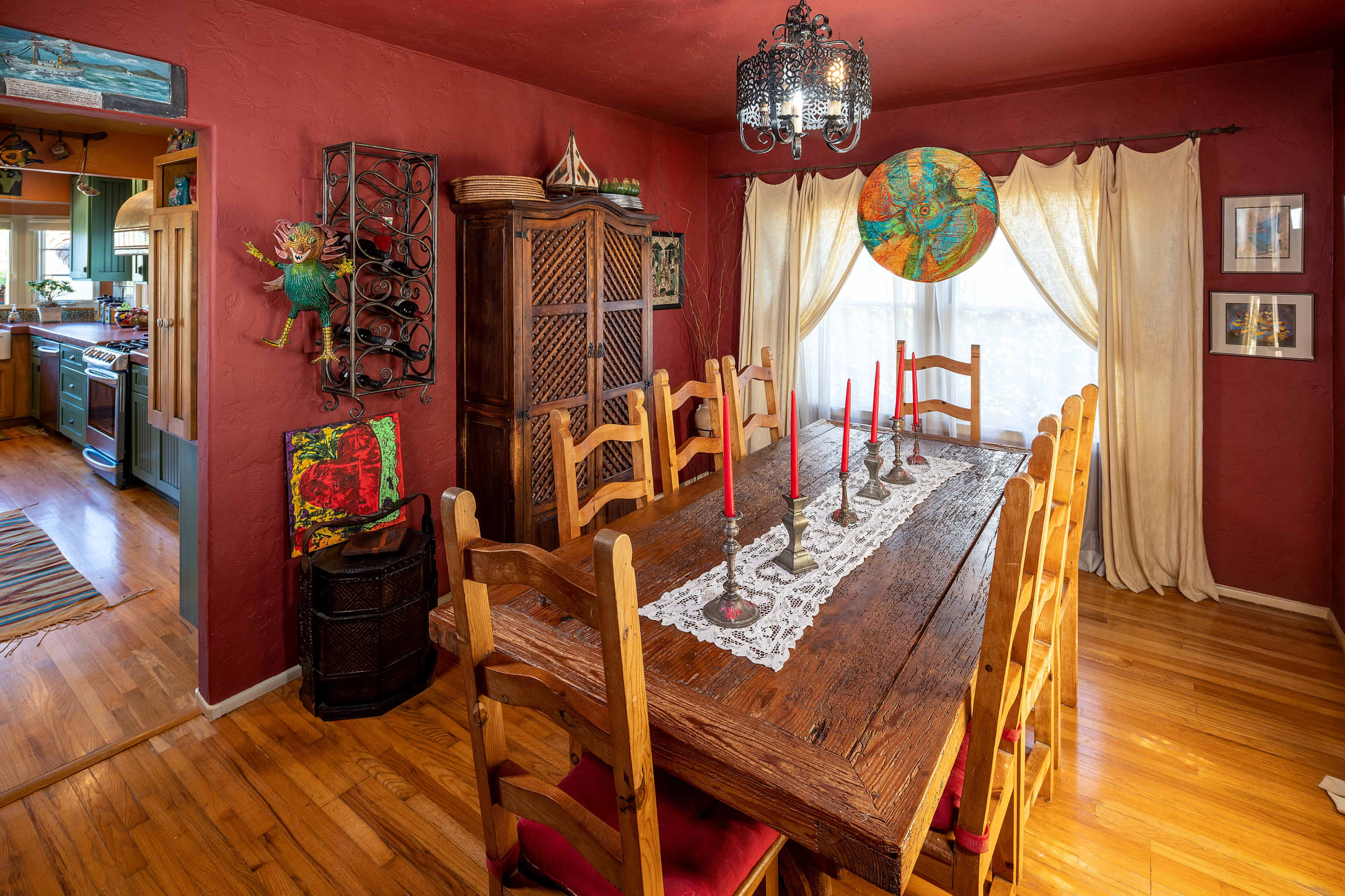 A wooden dining table with candles is set in a room with red walls, featuring a hanging chandelier and a globe on the wall.