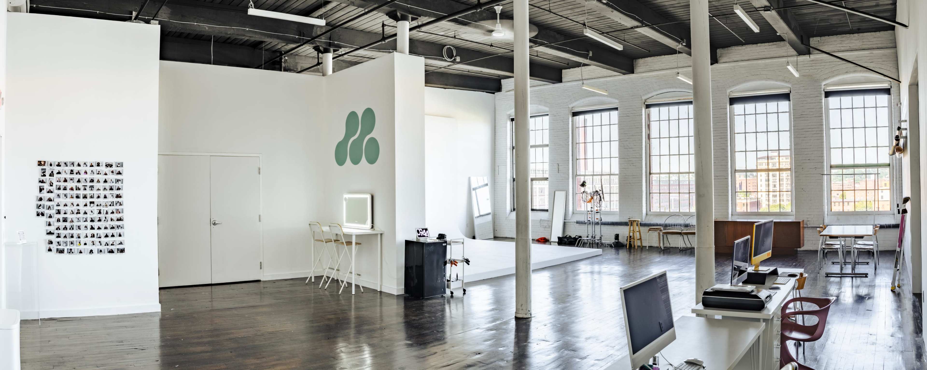 A spacious, well-lit studio with large windows, polished wooden floors, and minimalist furniture.
