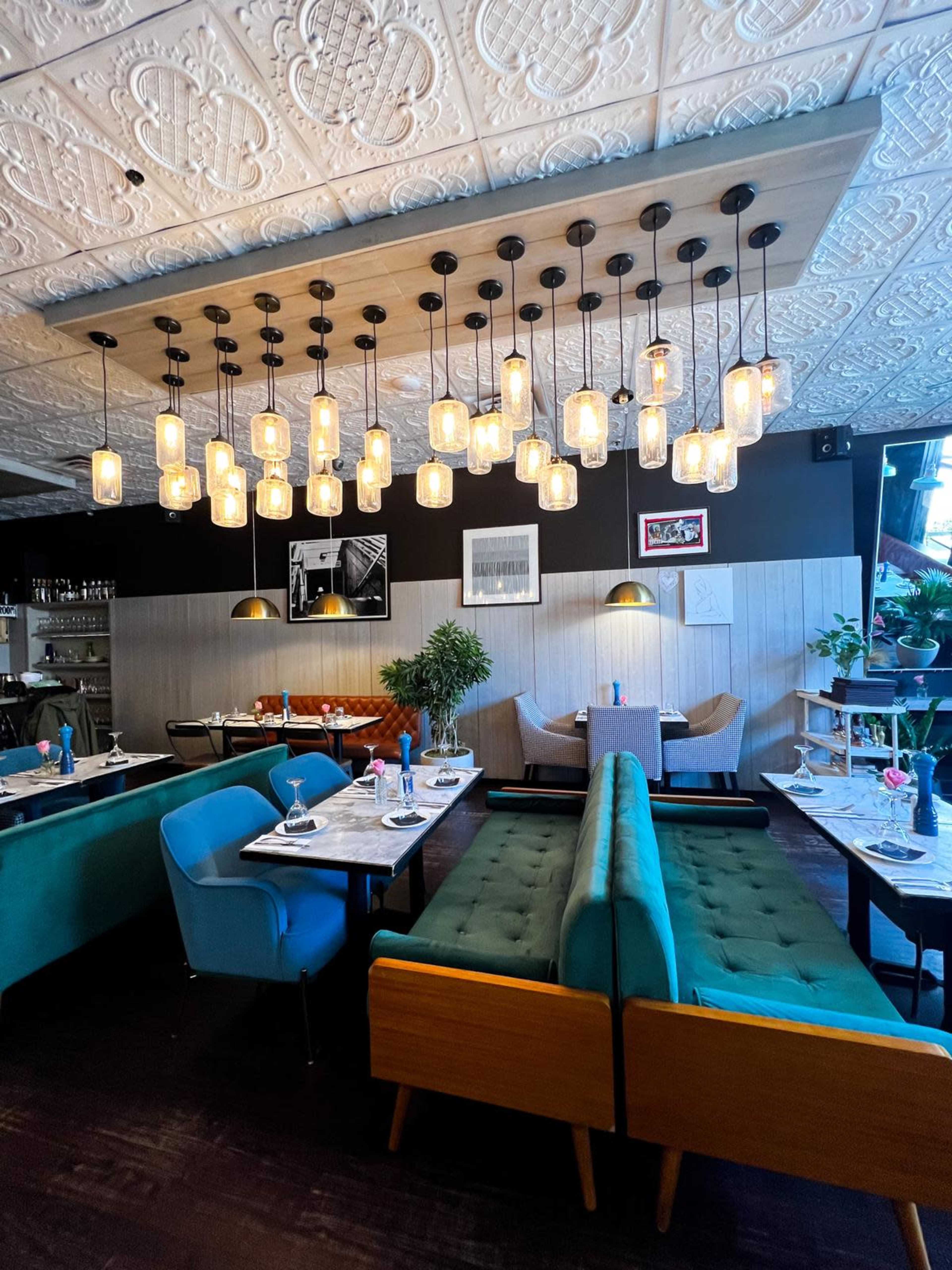 The image shows a modern restaurant interior with teal and wooden seating, decorative lighting fixtures, and neatly arranged dining tables.
