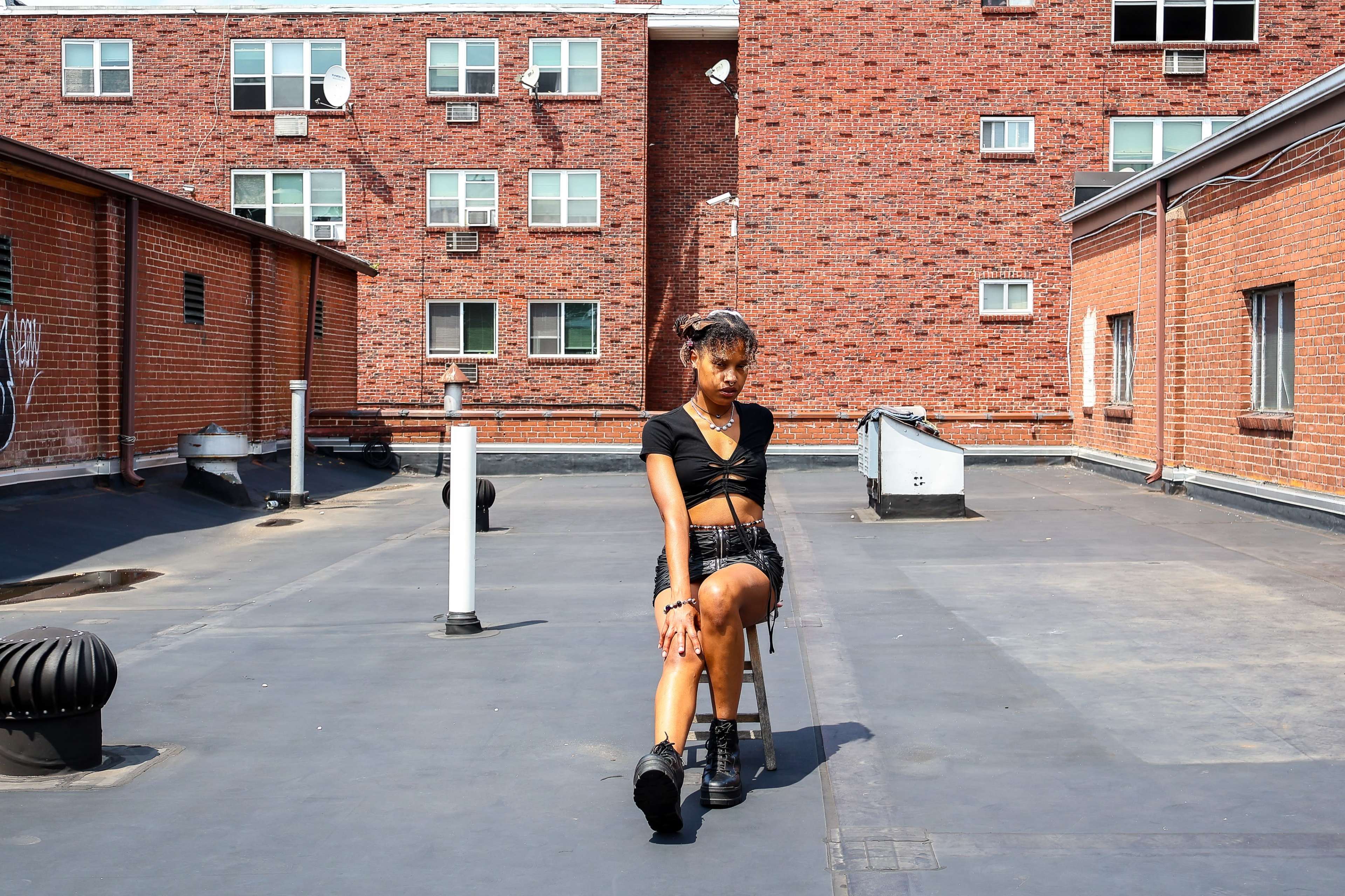 A person sits on a chair on a rooftop surrounded by brick buildings.