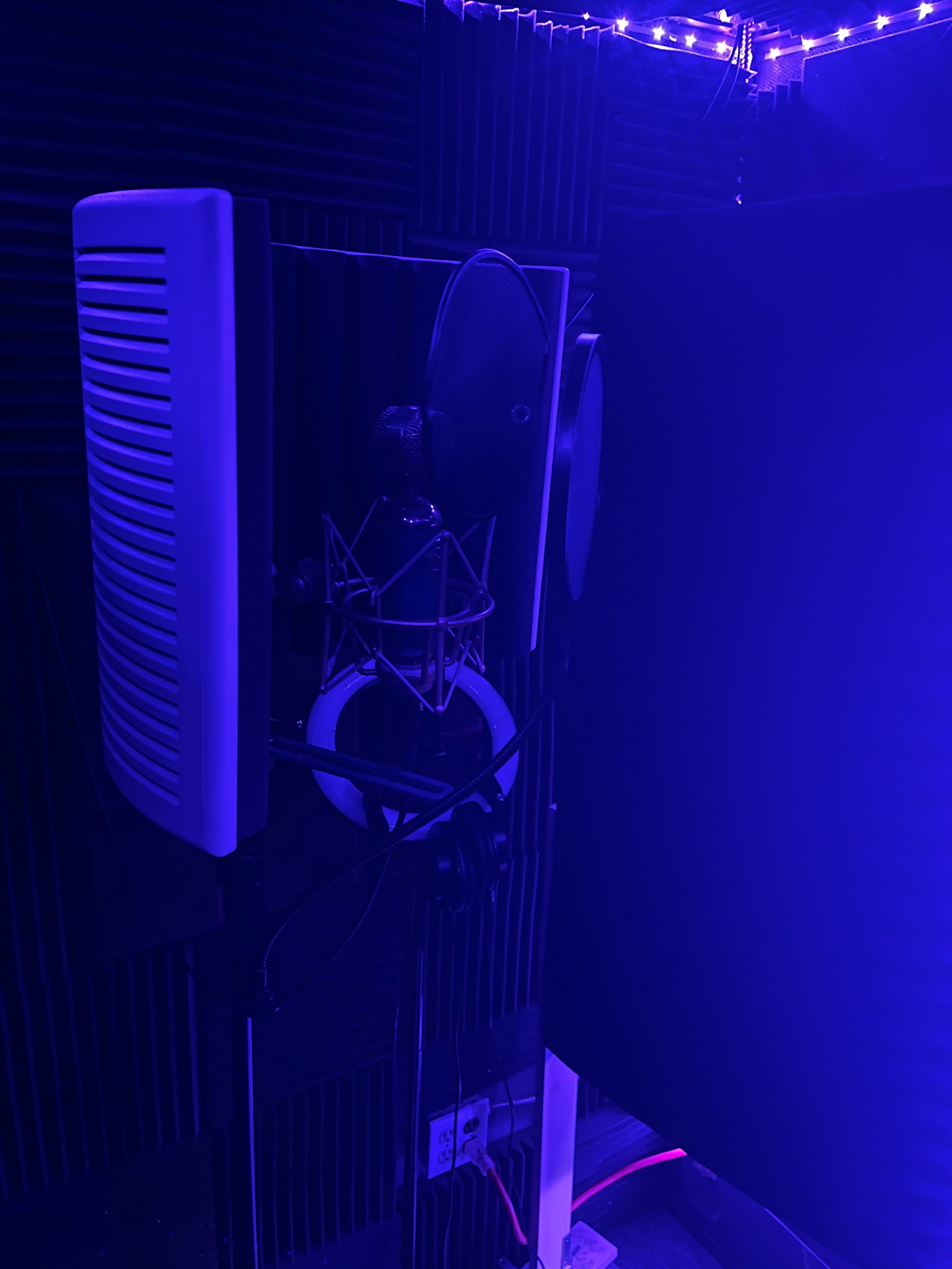 A recording studio setup with a microphone, a sound absorber panel, and ambient lighting.