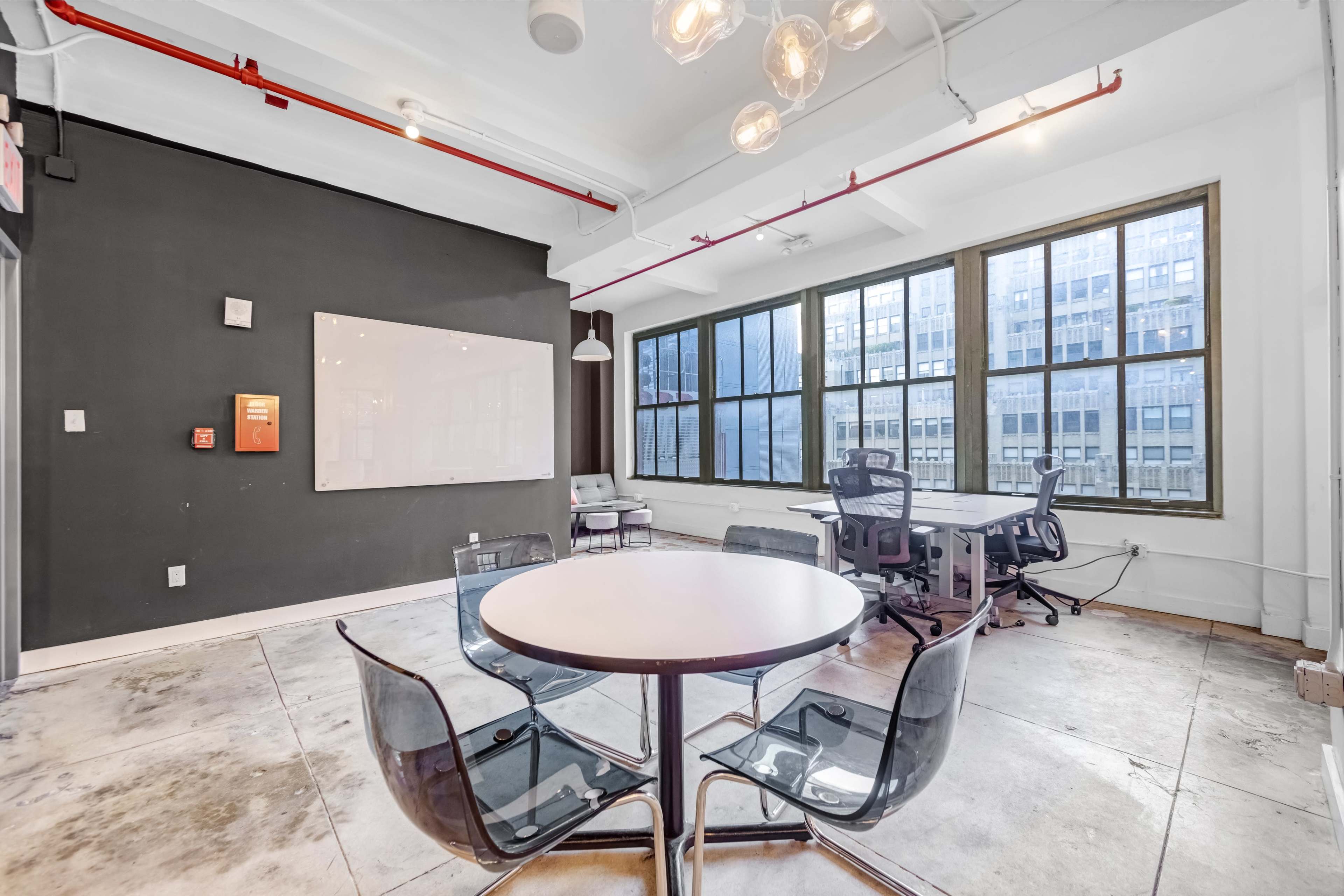 The image shows a modern office space with a round table and transparent chairs near large windows.
