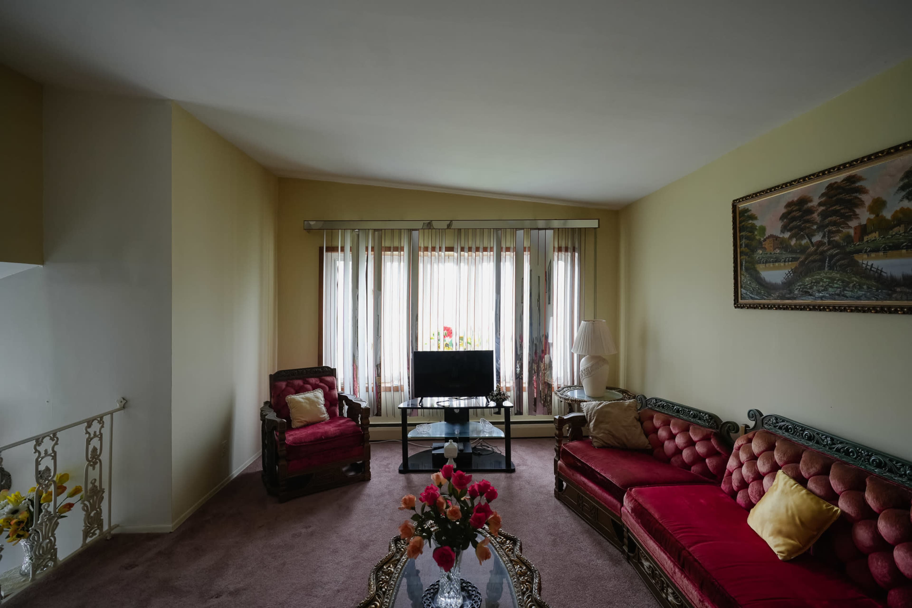 The living room features two red upholstered armchairs and a sofa arranged around a glass coffee table, with large windows letting in natural light.