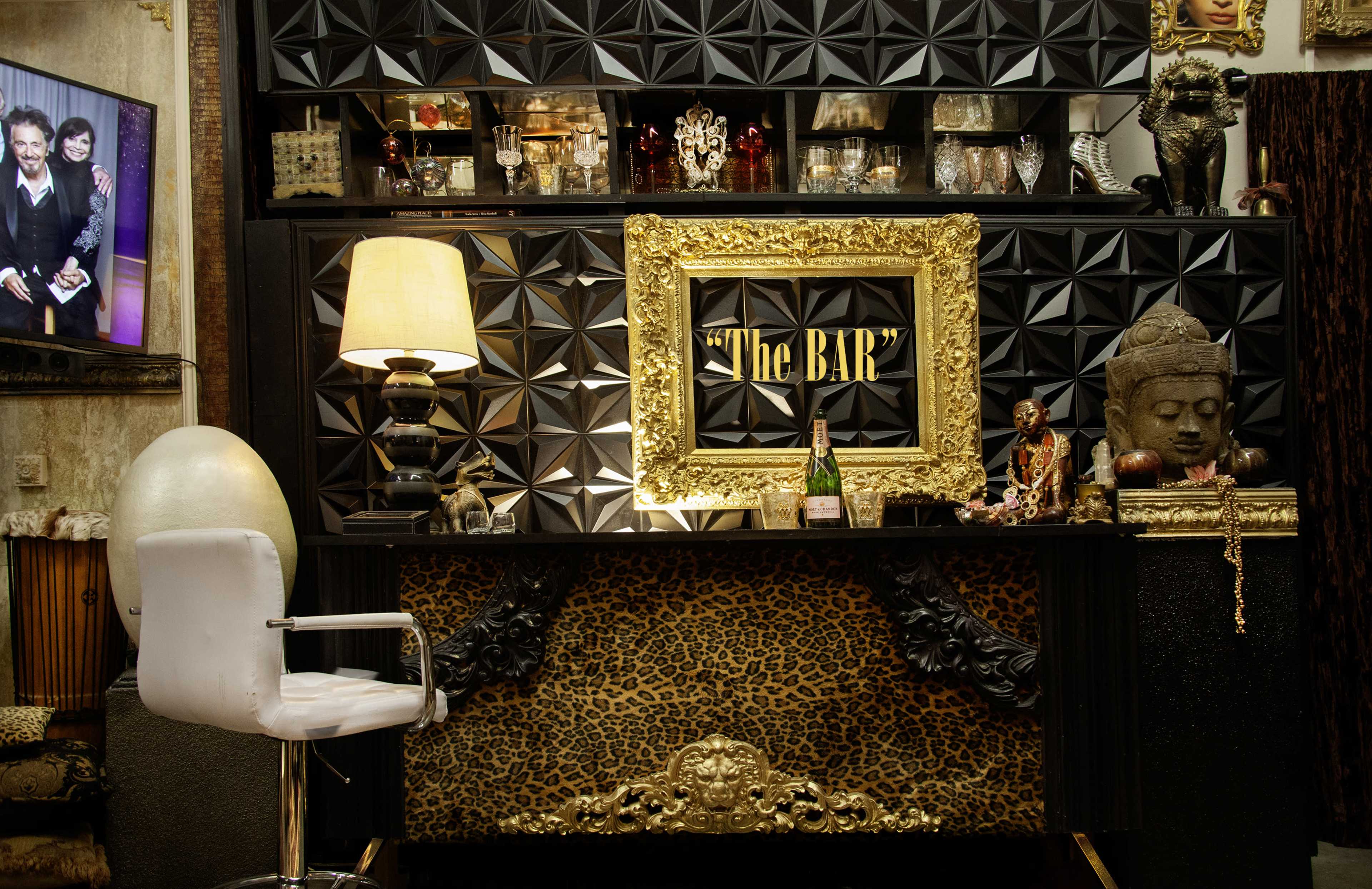 The image shows a stylish bar area with a decorative leopard-print front, a large gold-framed sign reading "The BAR," and various objects, including a lamp and a statue, arranged on the shelves behind it.