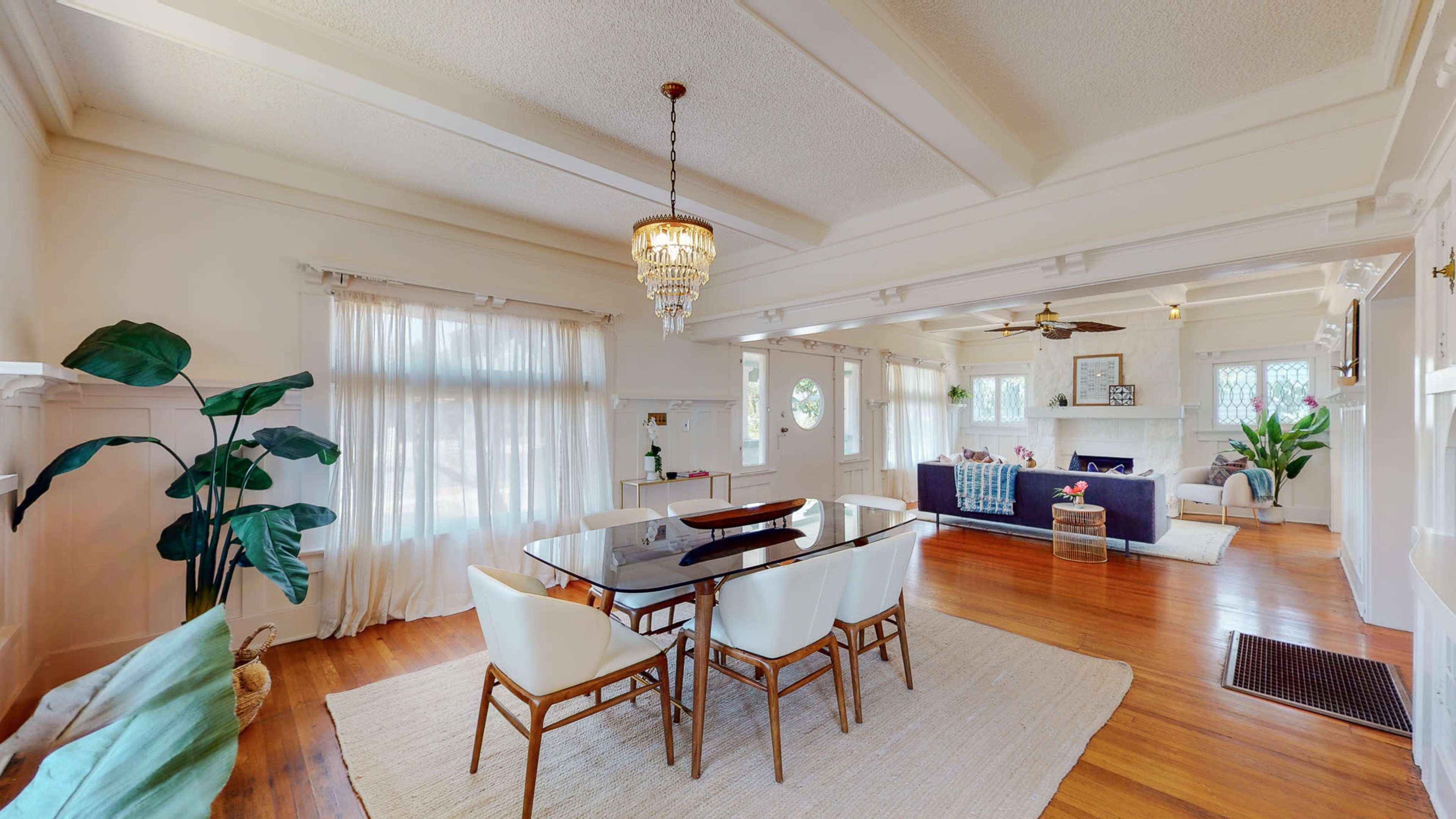 The image shows a spacious living and dining area with large windows, a dining table set for six, and a comfortable seating arrangement featuring a sofa and decorative elements.